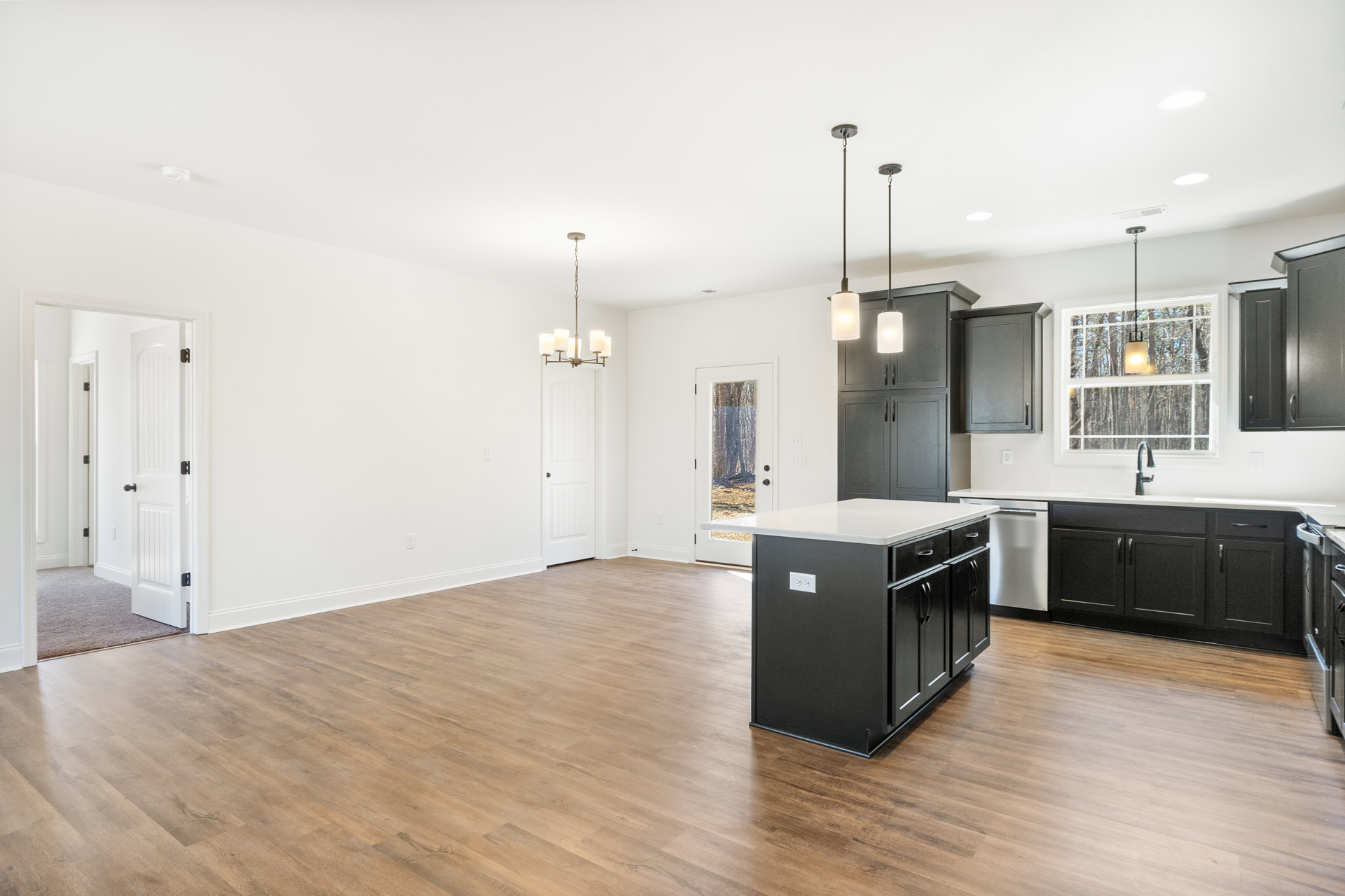 Open kitchen and dining area with hardwood flooring, white cabinetry, kitchen island featuring a white countertop, black counters, ceiling light fixture, white doors with black