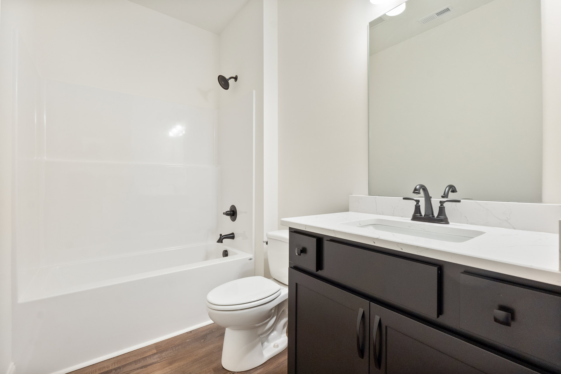 Bathroom with white toilet, modern sink and faucet, large mirror above vanity, tiled walls, and shower head with blue accent strip