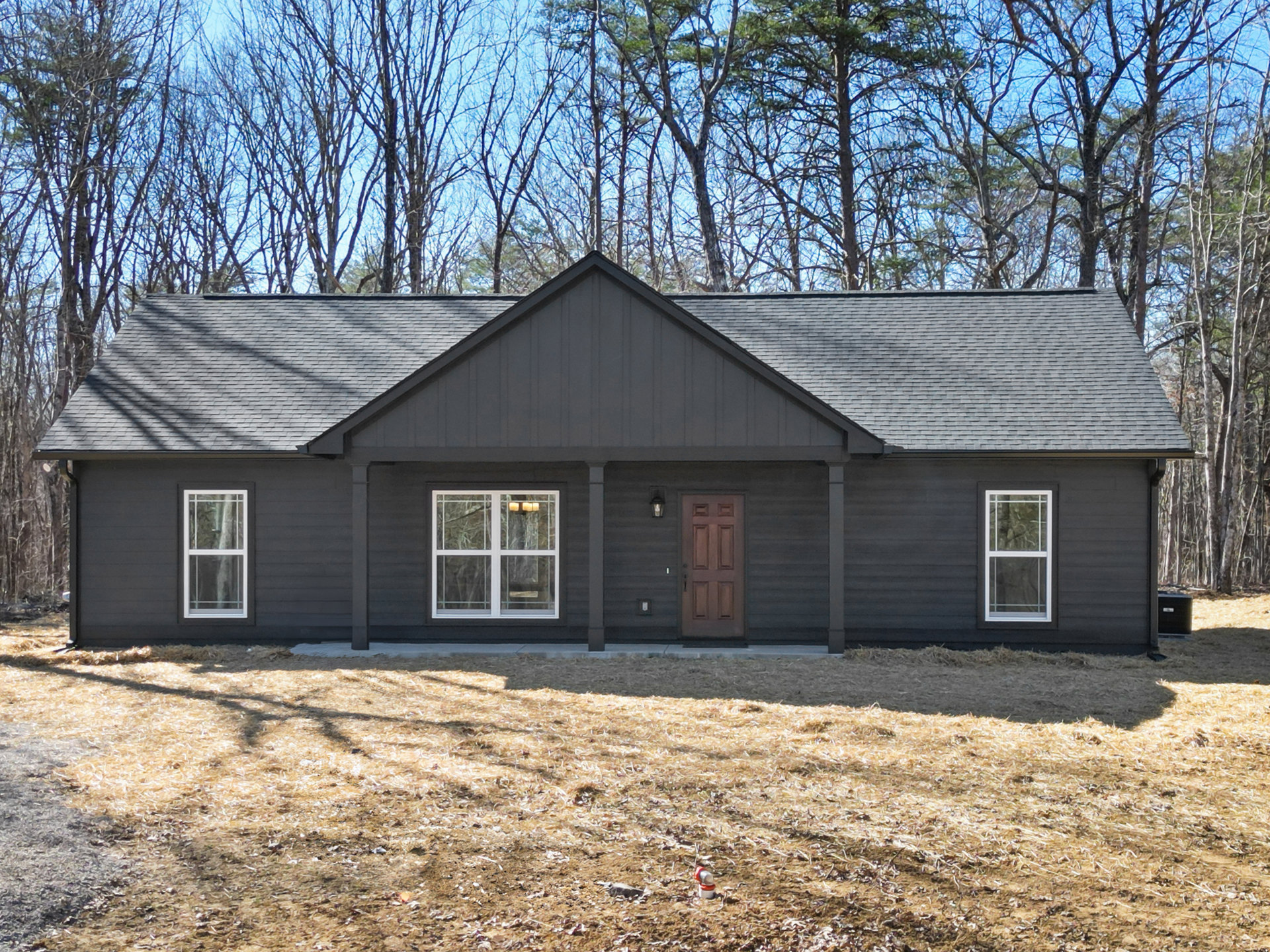 Brown shingle roof, white-framed window, wood front door, fire hydrant on grassy lawn, mature trees behind house