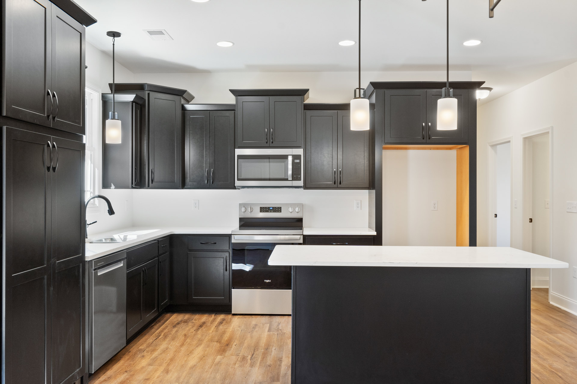 Black kitchen cabinets with white countertops, stainless steel oven and microwave, light-colored flooring, and modern sink fixtures.