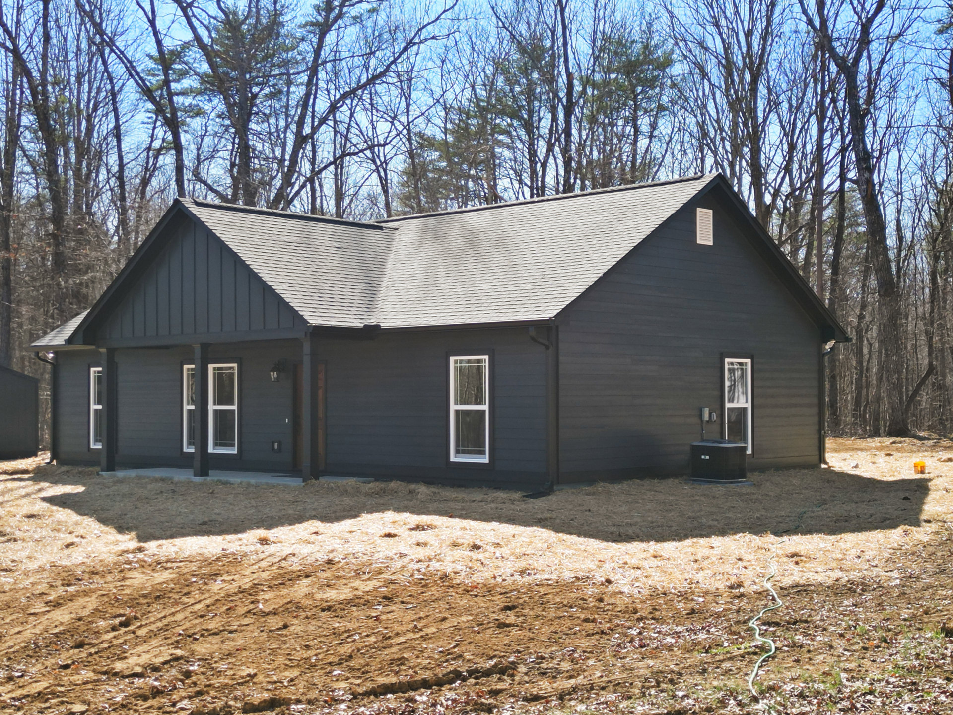 Two-story house with light siding, large windows, and a dirt patch in the backyard, surrounded by mature trees.
