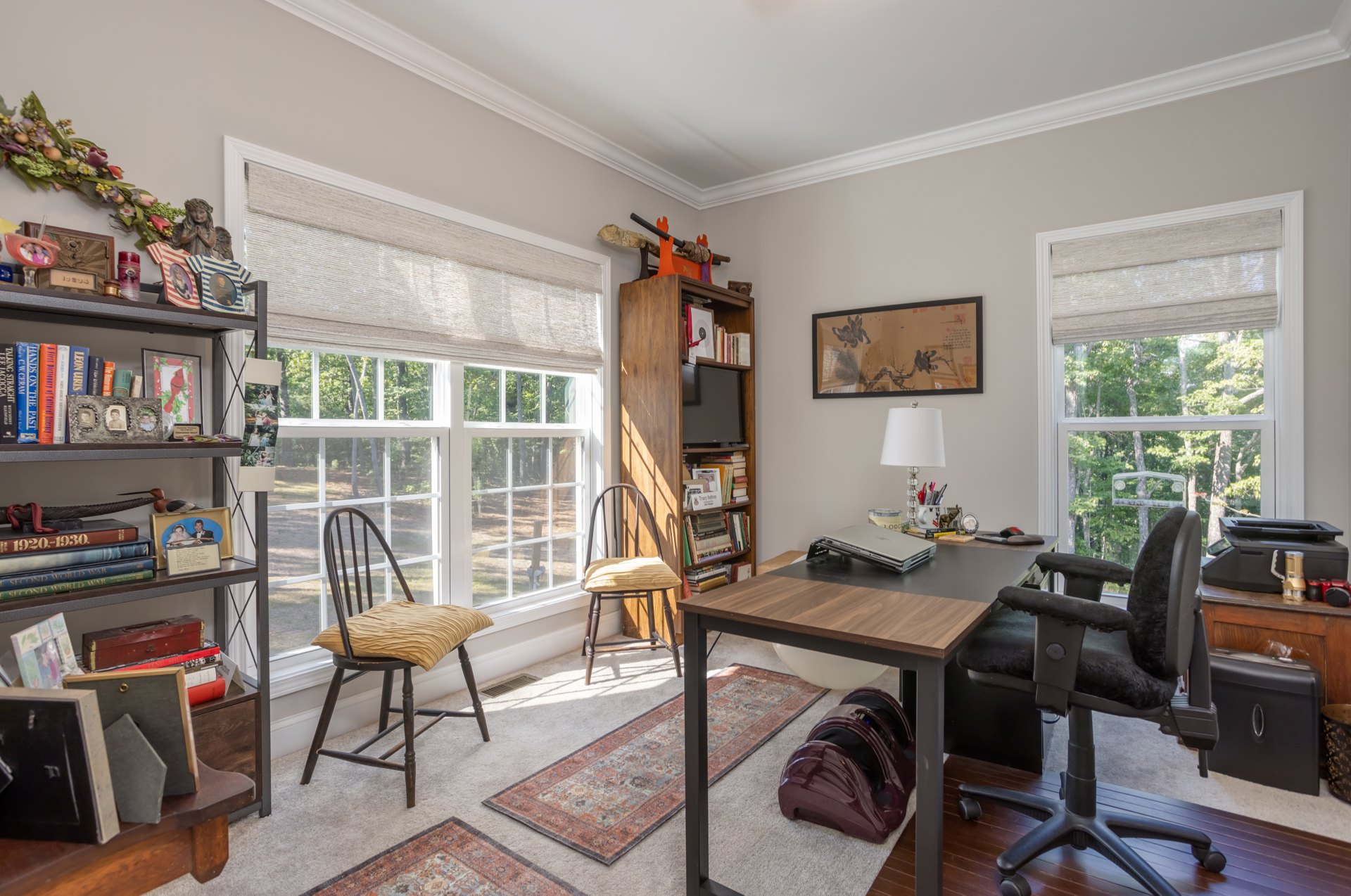Light-filled den with wood desk, black chairs with cushions, framed bird artwork on wall, purple decorative object on carpet, neutral cabinetry and flooring