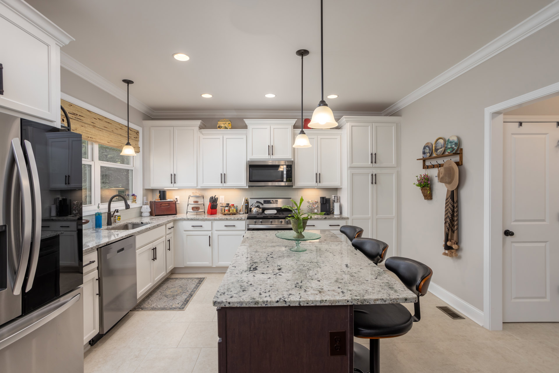 Spacious kitchen featuring a marble island countertop with a green plant in a glass bowl, modern cabinetry, built-in microwave, stacked bowls on open shelving, and a decorative