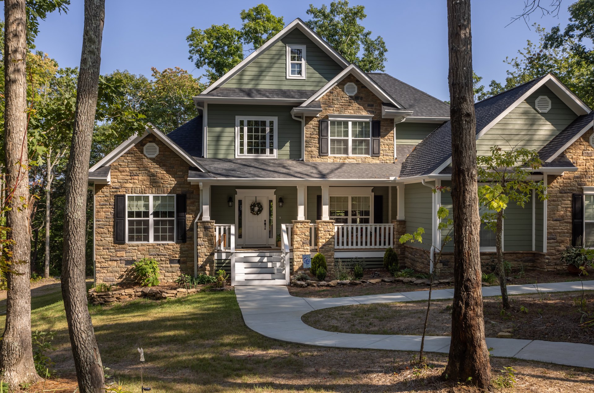 Modern grey house with white-framed windows, paved driveway, front porch, and mature trees in landscaped yard