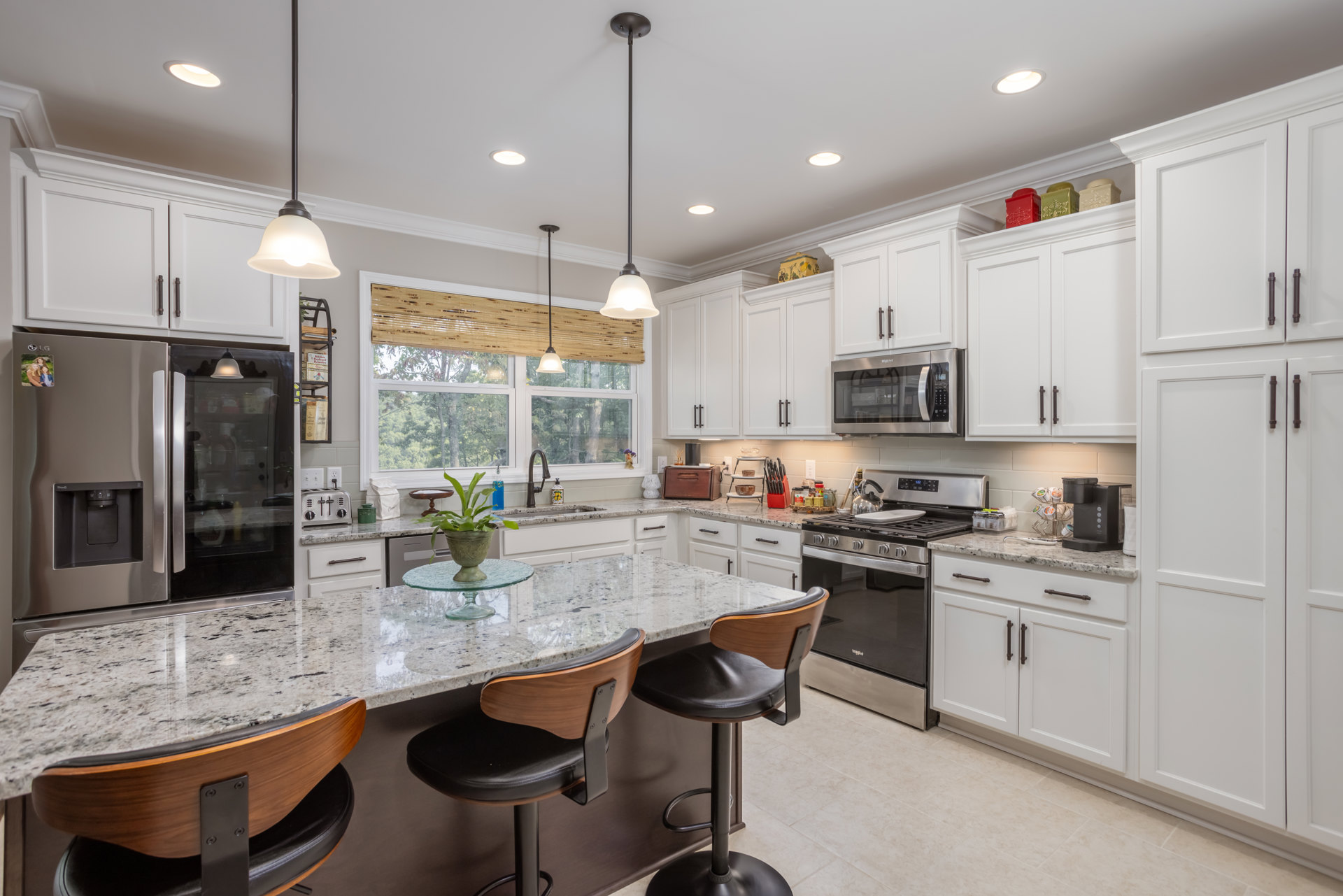 White kitchen cabinets with granite countertops, stainless steel stove and oven, glass door microwave, potted plant on counter, close-up of drawer, chair tucked under peninsula.