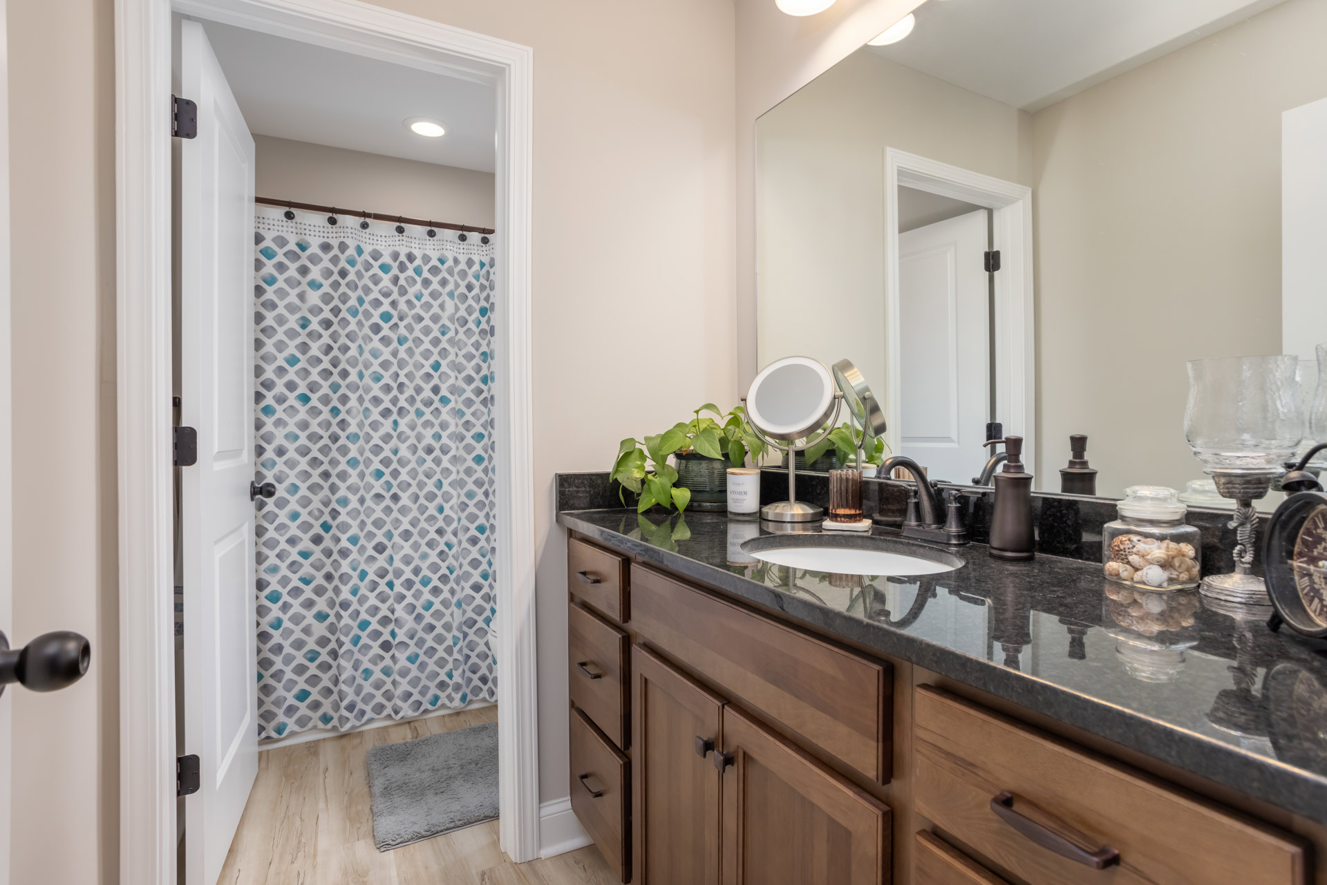 Modern bathroom featuring a rectangular mirror above a white sink with chrome faucet, light gray tile backsplash, dark wood cabinetry, and a white door adjacent to a shower with a
