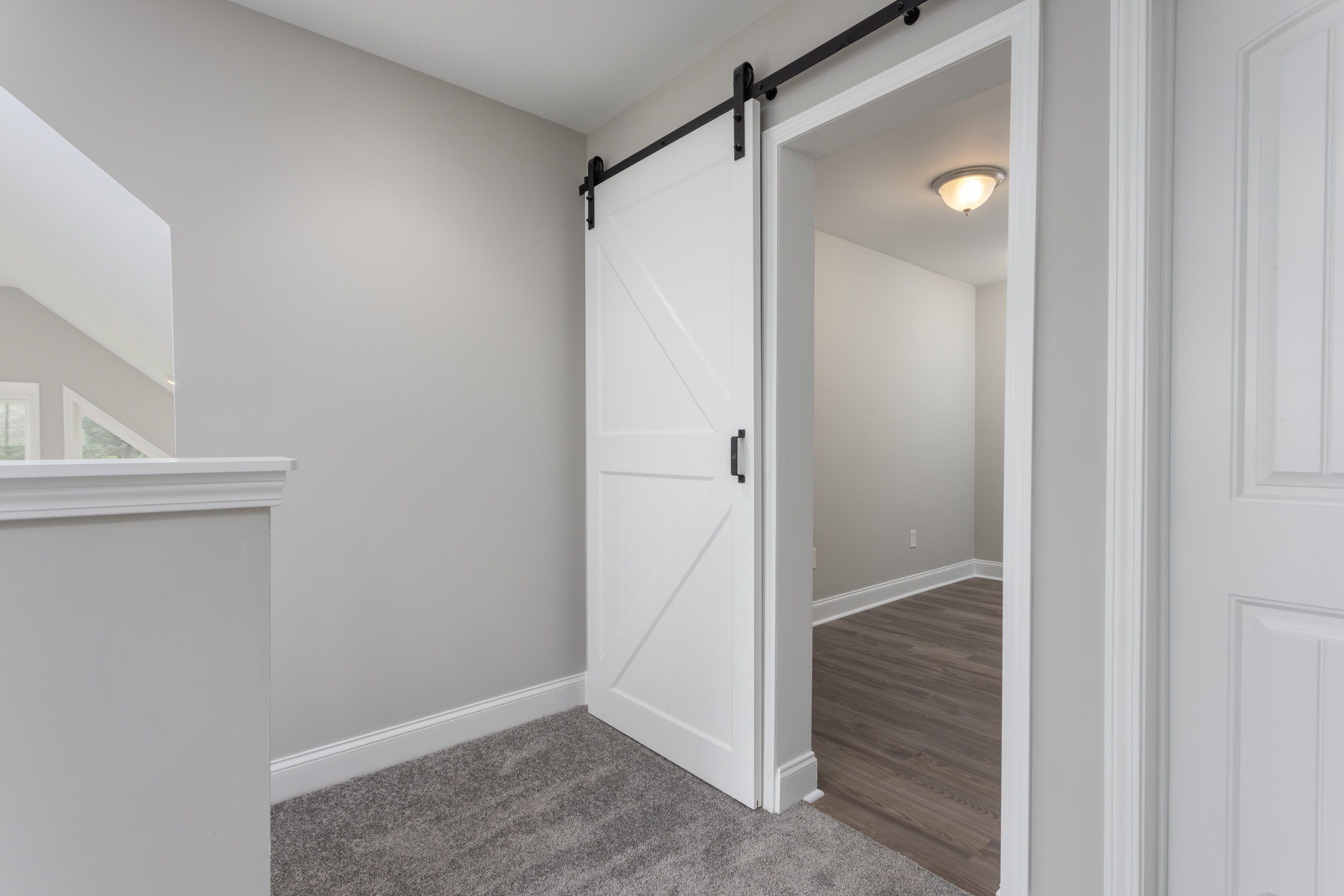 White sliding door with black border, wood floor with white trim, white ceiling featuring recessed light fixture, white walls in modern room.