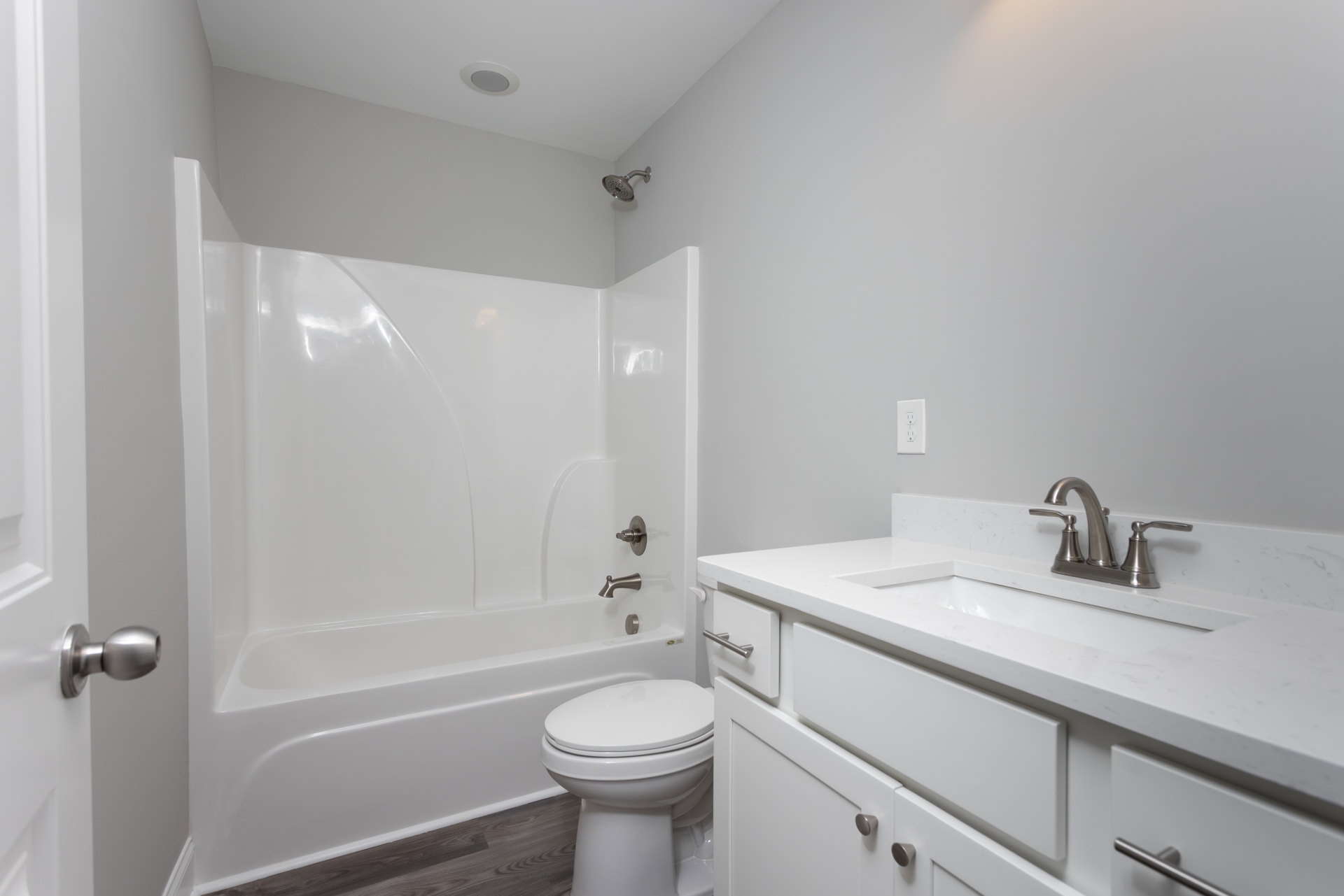 Modern bathroom with white toilet, rectangular sink on wood vanity, wall-mounted faucet, light gray tile flooring, and glass-enclosed shower with chrome showerhead