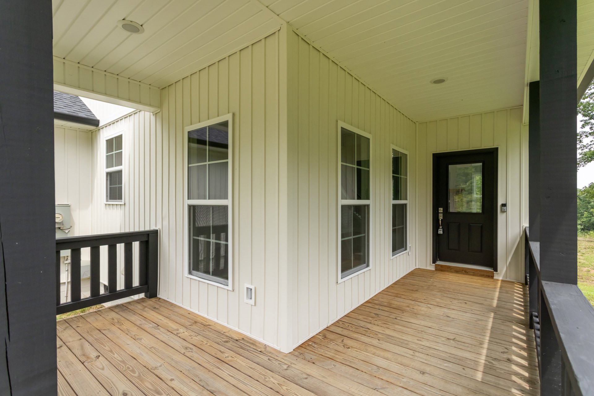 White siding house with black front door, wooden deck, white framed windows, and black metal railing