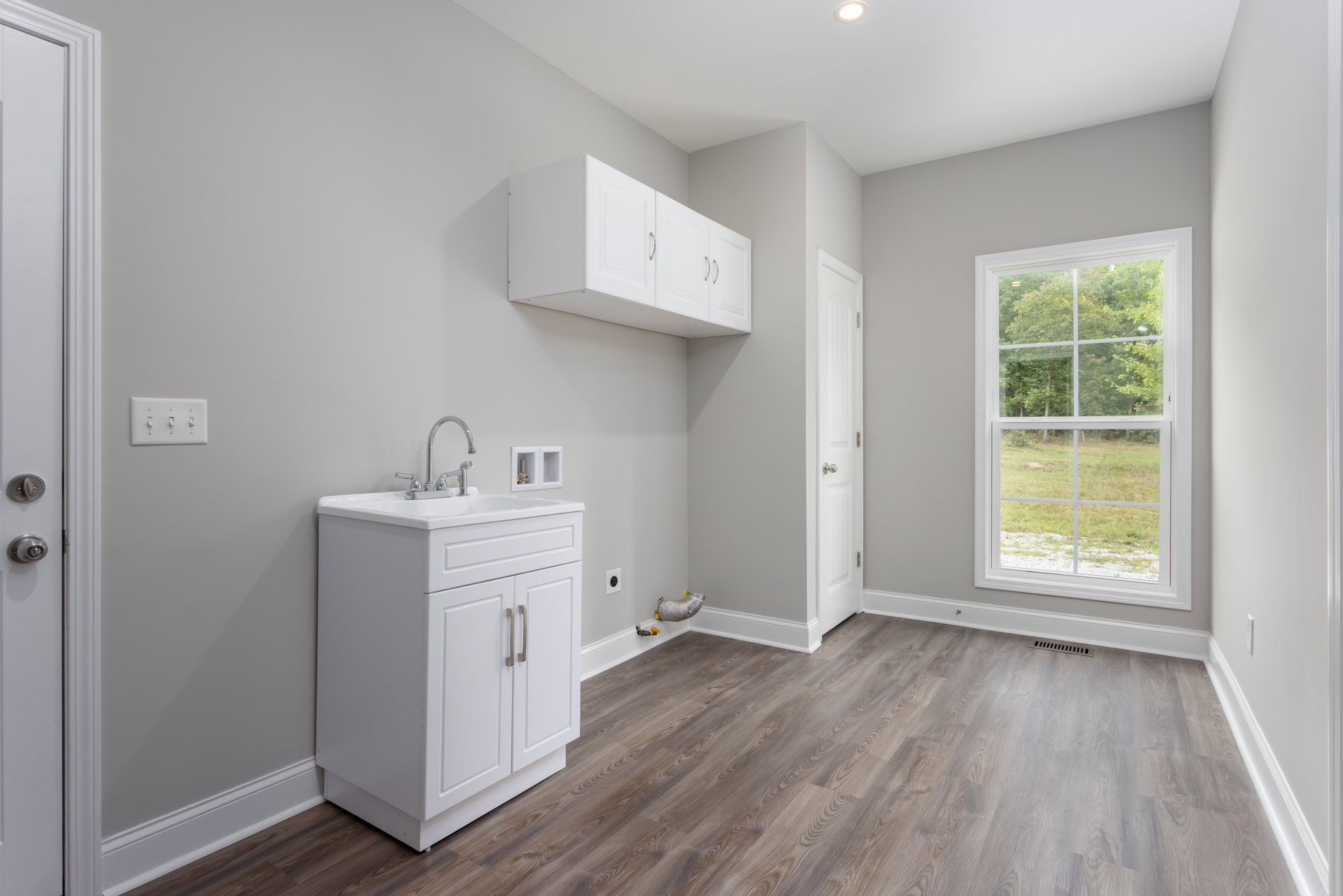 White cabinets and drawers with a built-in sink, silver pipe with yellow tags mounted on the wall, window overlooking trees, row of wall switches, white rectangular device with