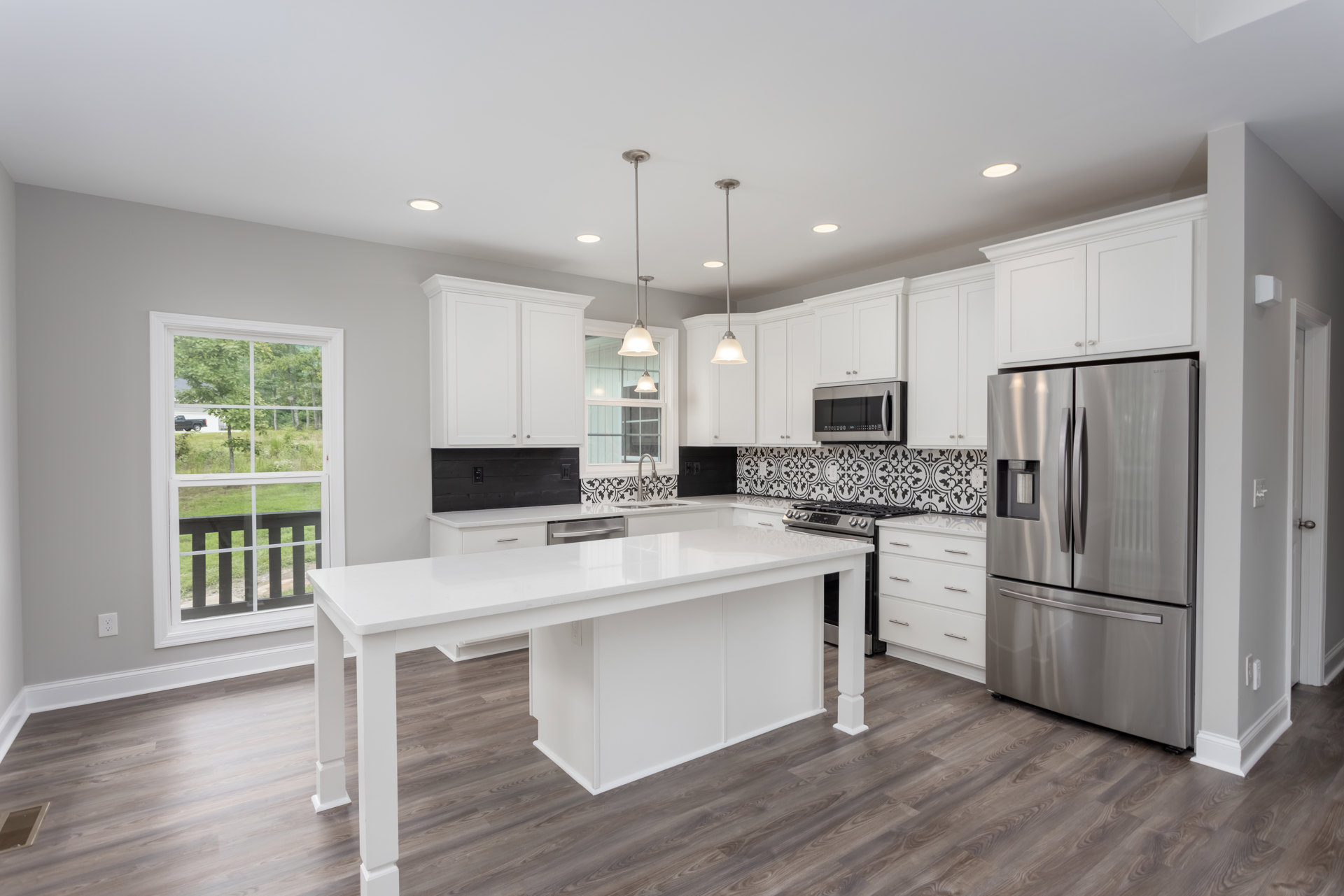 White kitchen with wood flooring, white cabinets, large white island, stainless steel refrigerator with water dispenser, built-in microwave, window overlooking fenced yard with