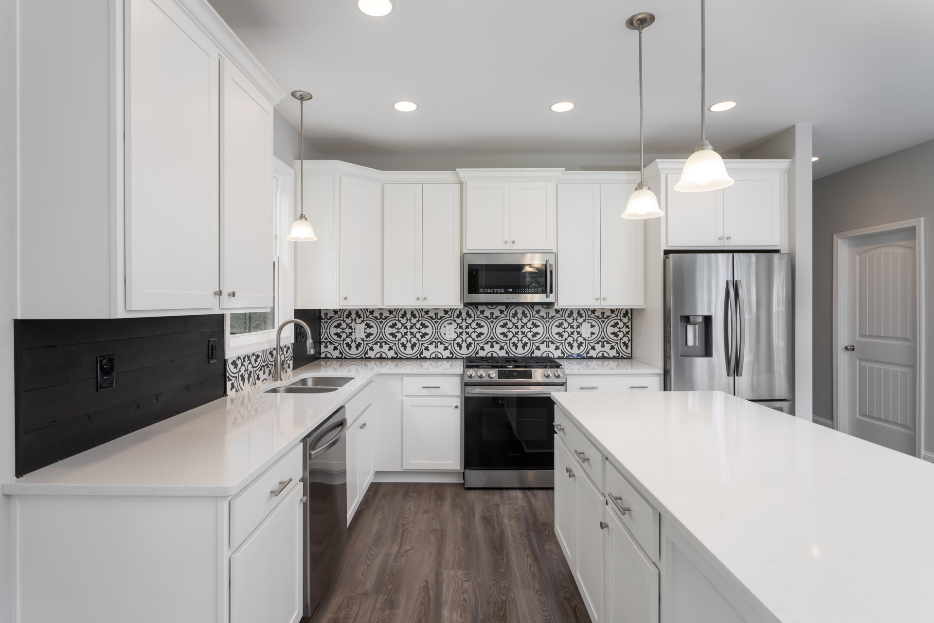 White kitchen cabinets and black and white tile backsplash, stainless steel refrigerator with water dispenser, stove and range on white countertop, microwave oven with light on