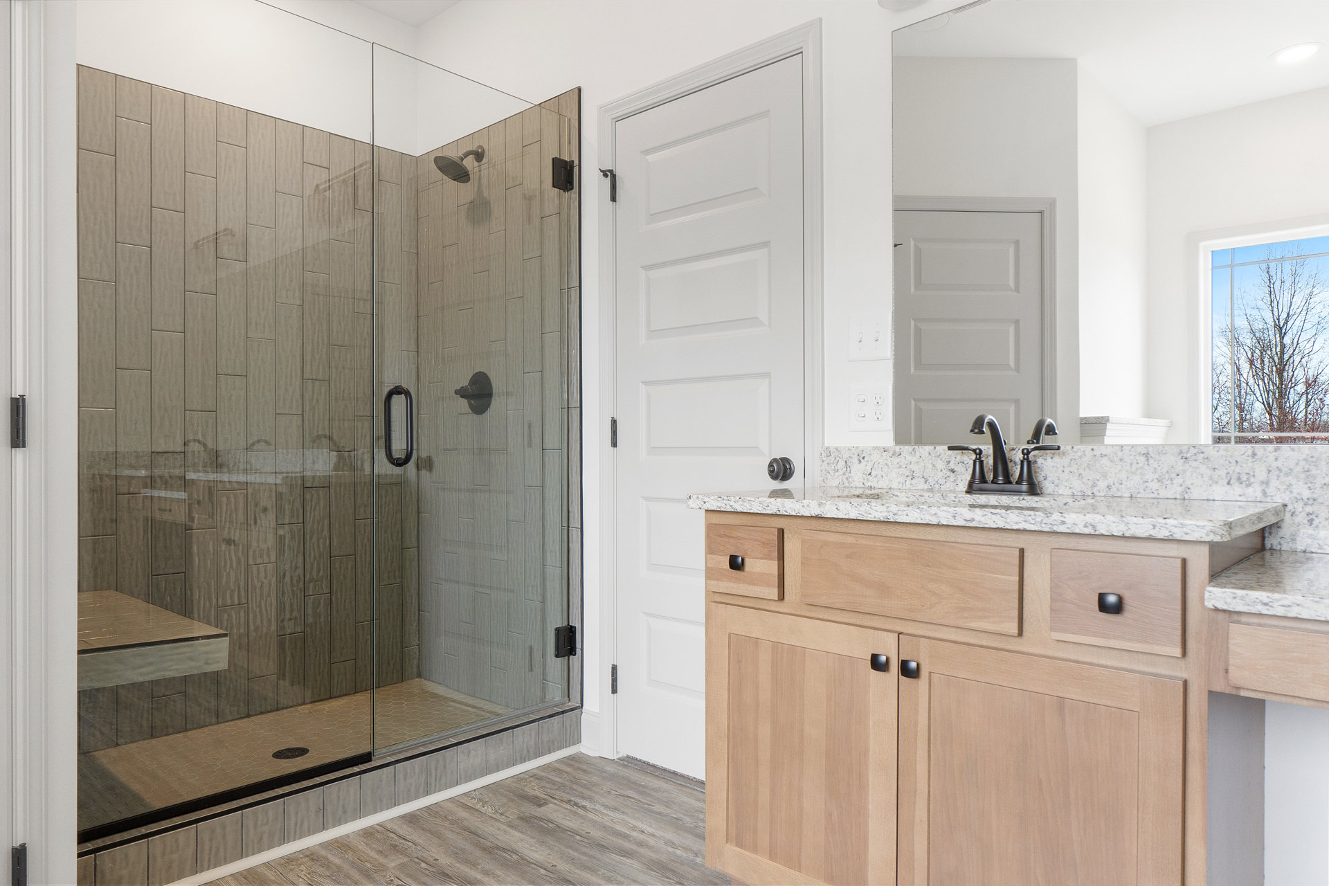 Bathroom featuring a glass shower with built-in bench, marble countertop sink, white door, and tree visible through window