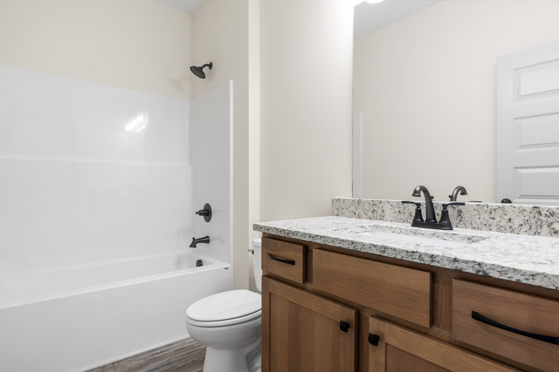 White bathroom featuring a wall-mounted sink with chrome faucet, glass-enclosed shower with blue accent band, white toilet with closed lid, and light tile flooring.