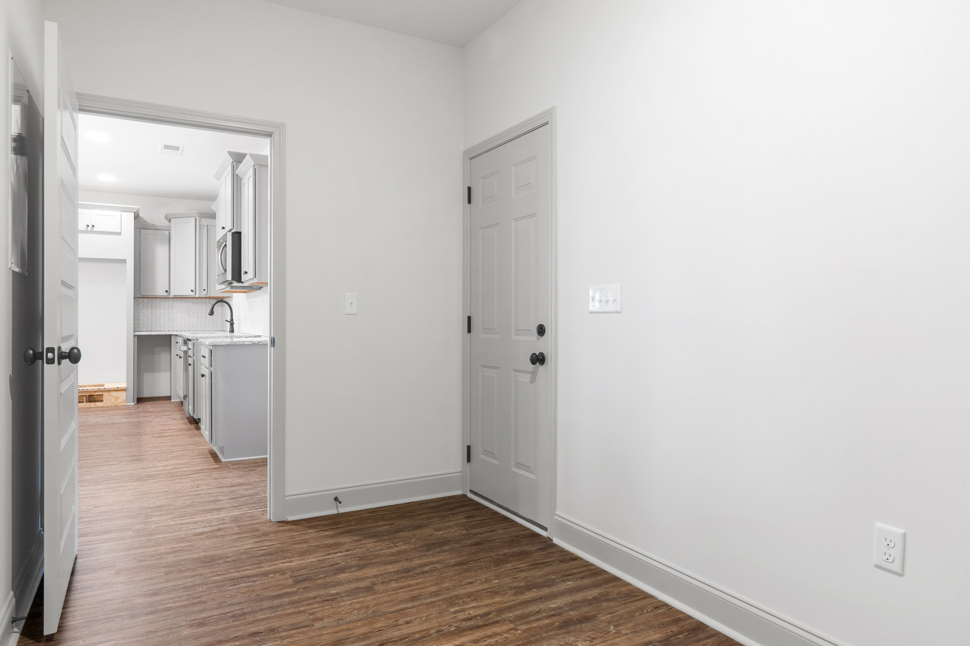 White paneled door with black handles set in a white wall, wood laminate flooring, white cabinet with black handles, four-switch white light switch, and close-up electrical outlet.