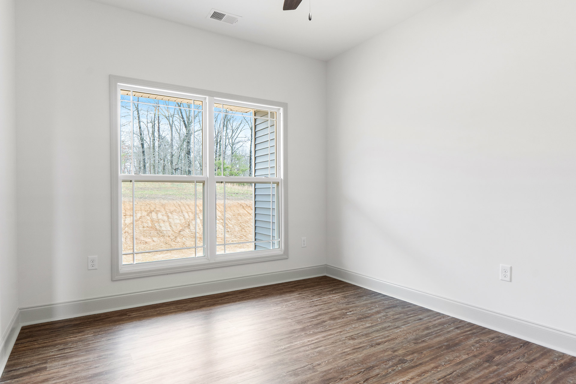 Sunlit room featuring wide plank wood flooring, plaster walls, and a large window overlooking a field and trees.