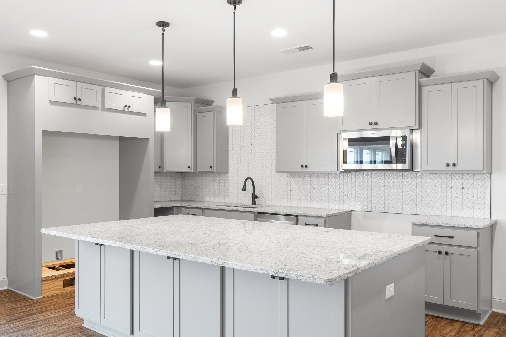Spacious kitchen featuring a large white island with wood accents, tile backsplash, built-in microwave, white countertops, modern cabinetry, stainless sink, and light fixtures.
