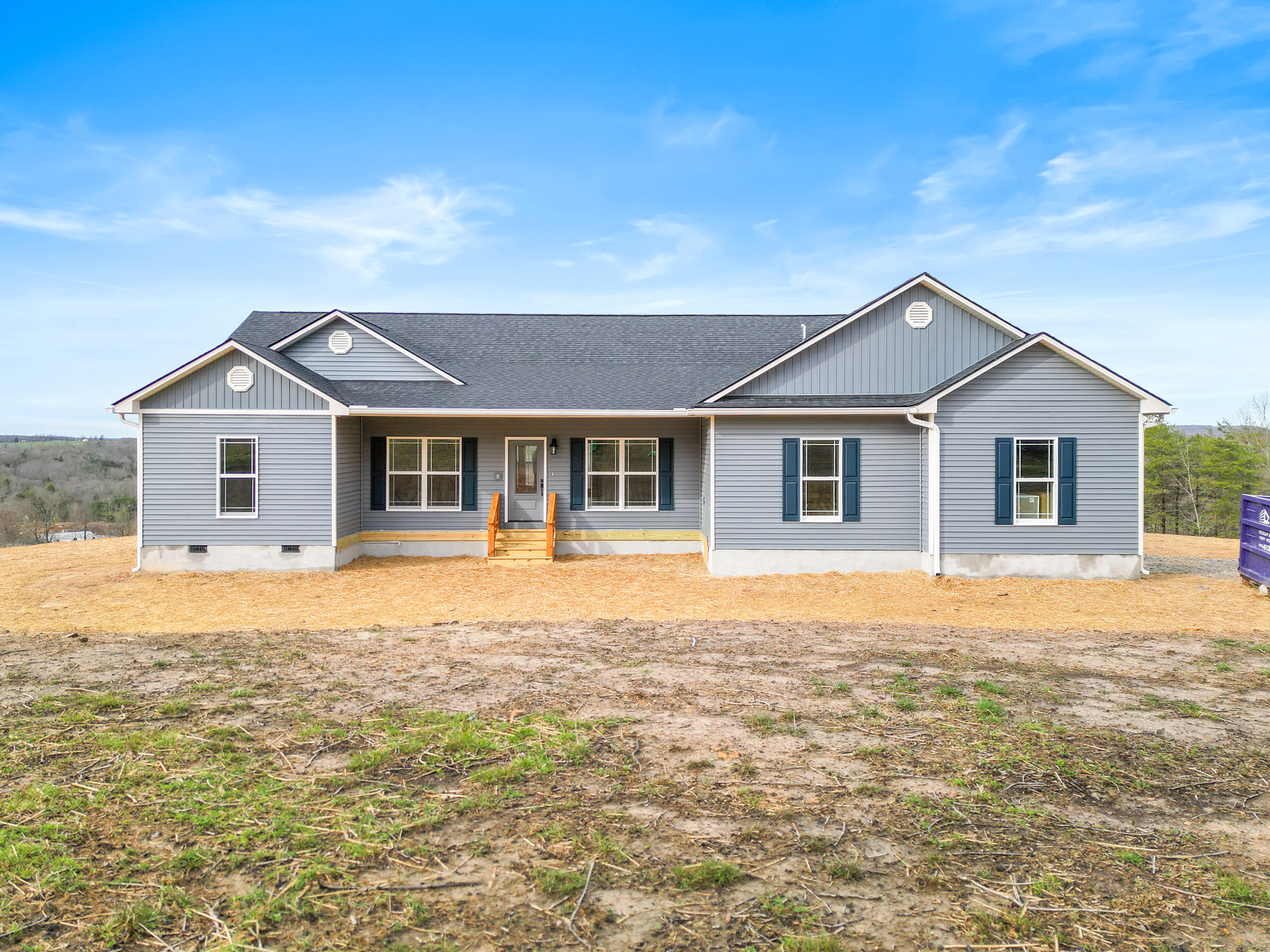 Two-story cottage with white siding, covered front porch, wooden steps, large windows, and landscaped yard under clear blue sky