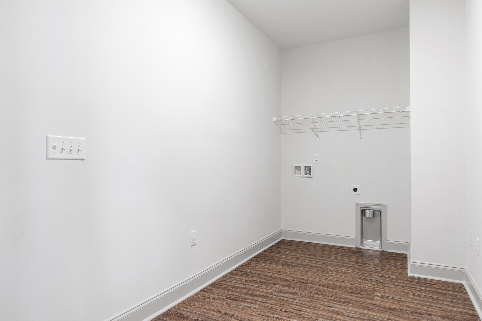 Wood floor with white plaster walls, row of electrical switches, metal water faucet, and white metal fence against white background.