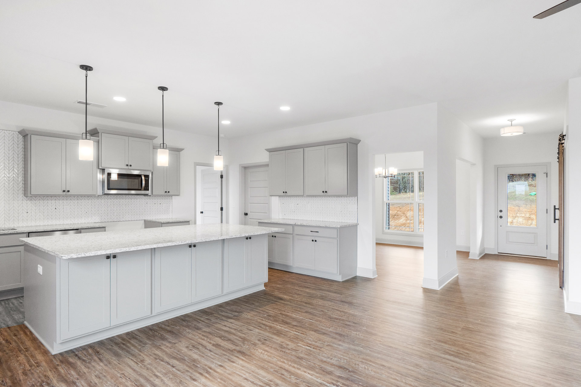 Open kitchen and dining area with white cabinets, white countertops, stainless microwave, hardwood flooring, and a white door featuring a glass window