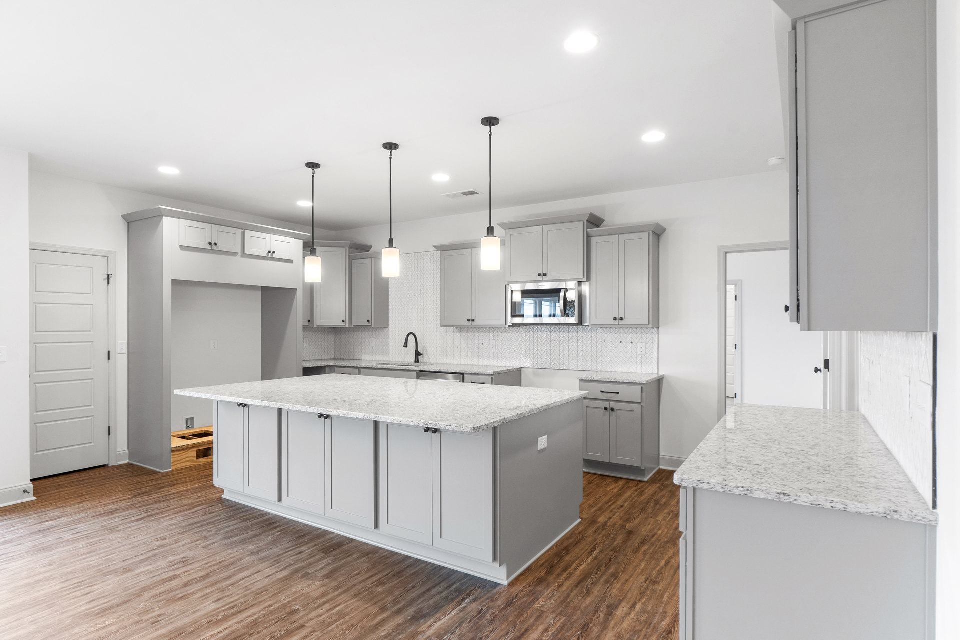 Kitchen with white cabinetry, marble island countertop, stainless steel microwave, white door with black handle, light wood flooring, and recessed ceiling lights