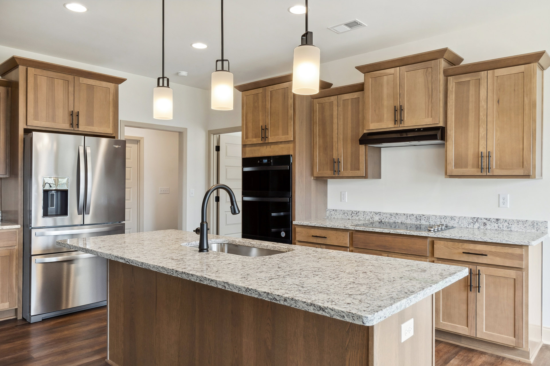 Marble kitchen island with built-in sink, stainless steel refrigerator featuring ice and water dispenser, white cabinetry, granite countertops, and modern lighting fixtures
