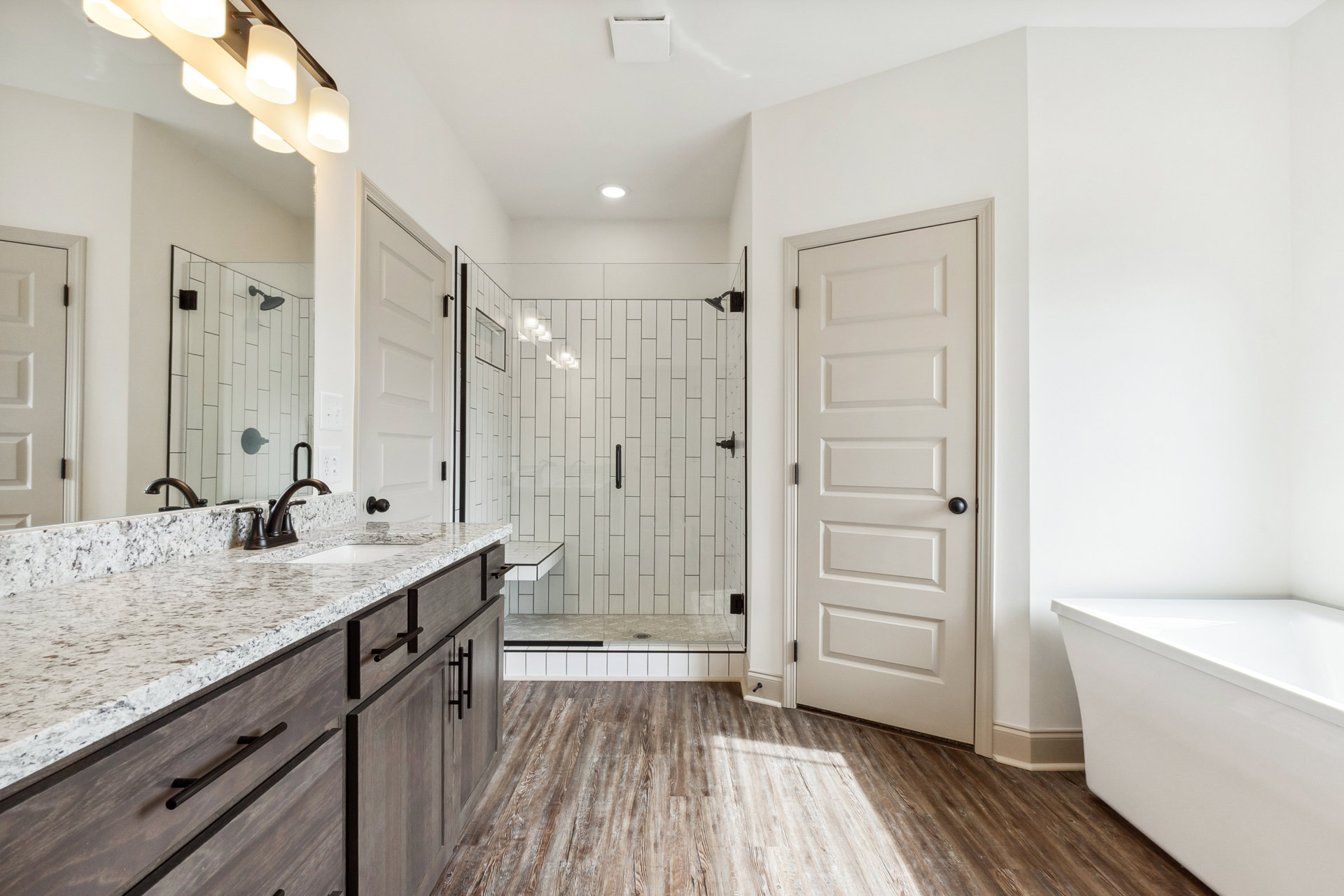 Bathroom featuring a marble countertop with undermount sink, frameless mirror, white bathtub, tiled shower wall with chrome showerhead, and white door with black hardware