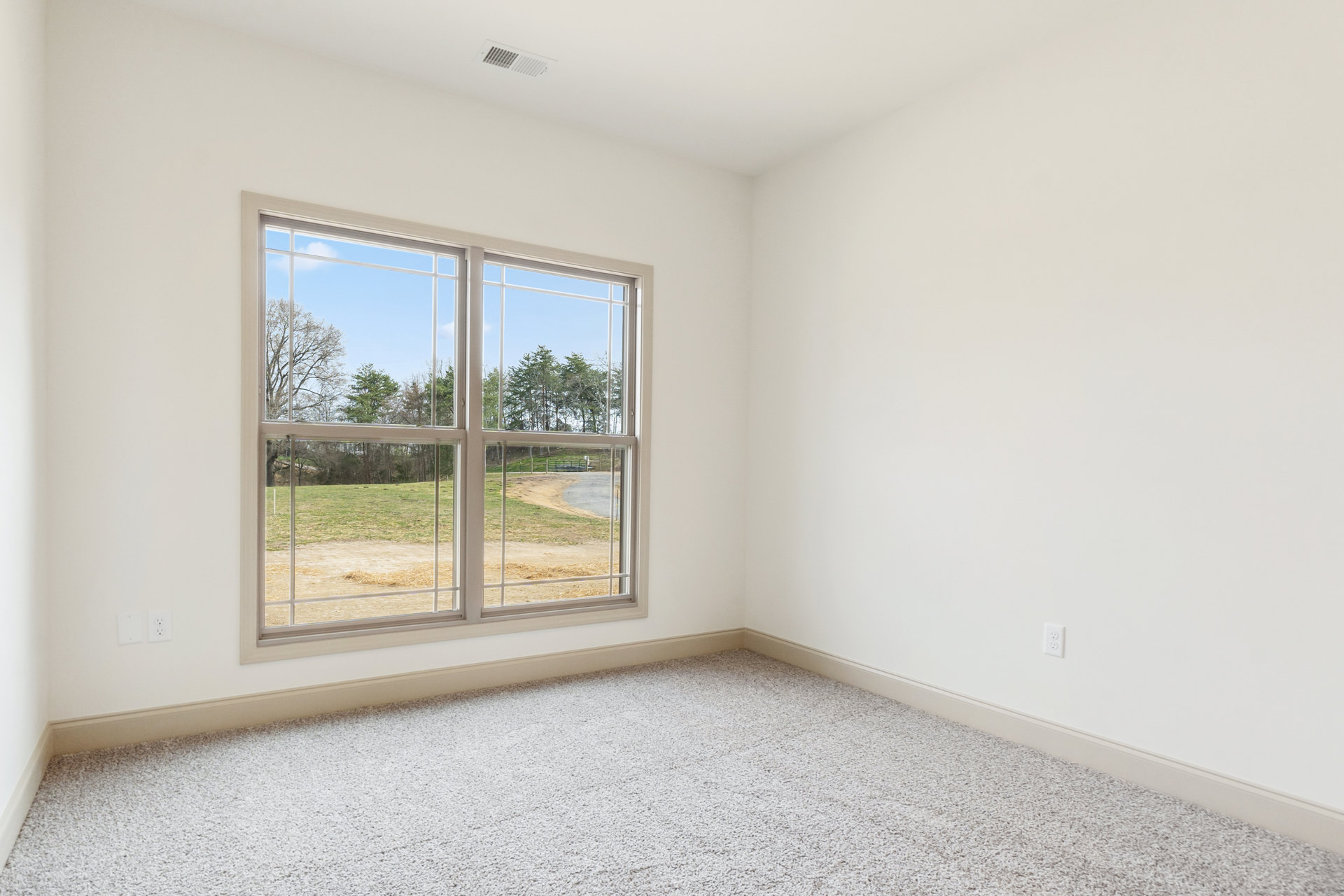 Carpeted floor in a bright room with a large window overlooking grass and trees