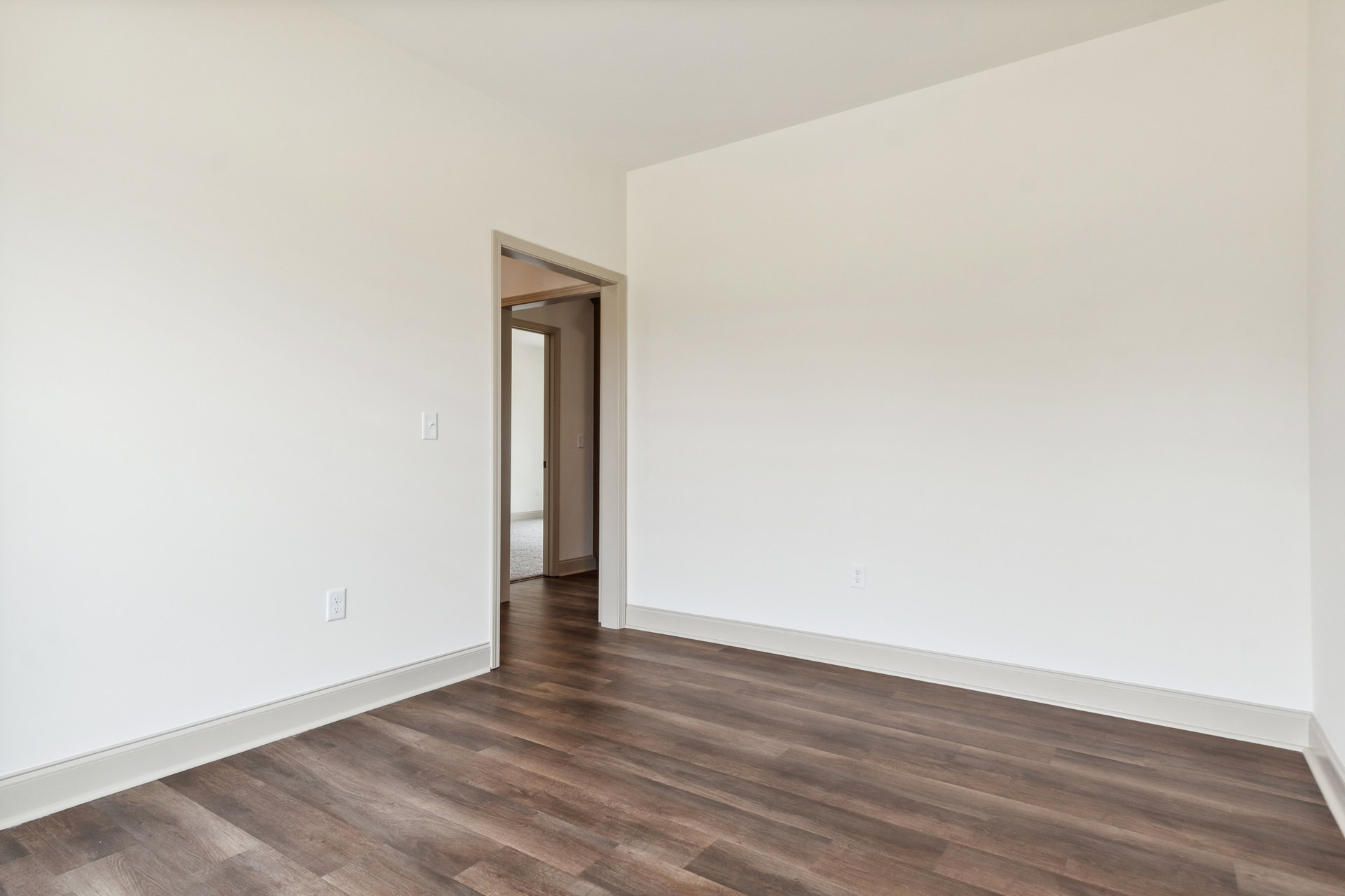 Wood flooring with white trim, white walls, and an open white door leading to another room