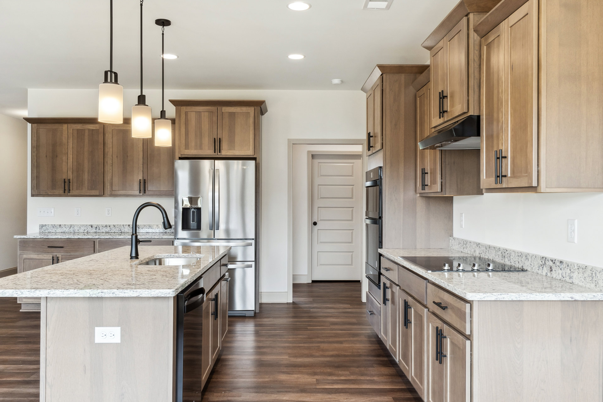 Kitchen with natural wood cabinets, granite countertops, stainless steel refrigerator, central island featuring a sink with black faucet, white door with black handle, and modern