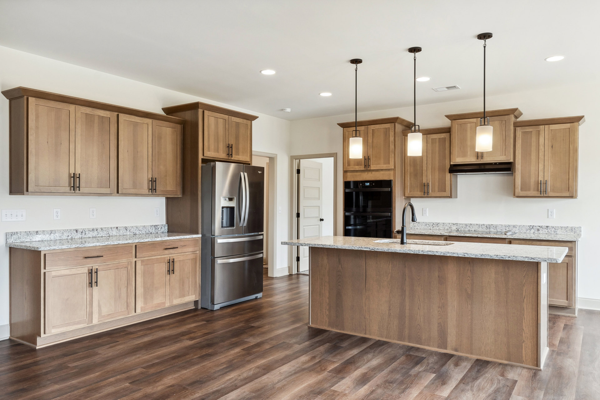 Kitchen featuring wood cabinetry, stainless steel double-door refrigerator, black oven with digital display, stone countertop with built-in sink, and modern central light fixture