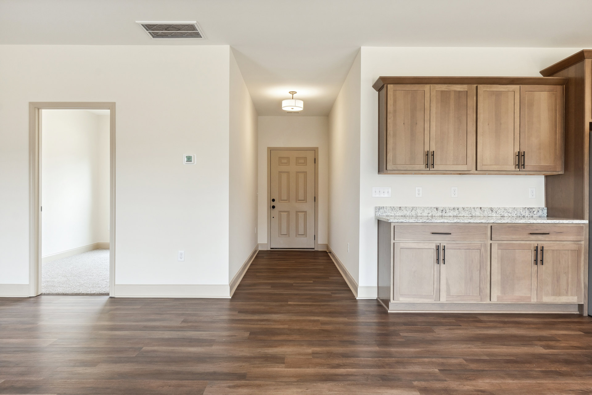 Wood flooring and white walls in a kitchen with white cabinetry, black hardware, white door with matching frame, and a white-shaded light fixture