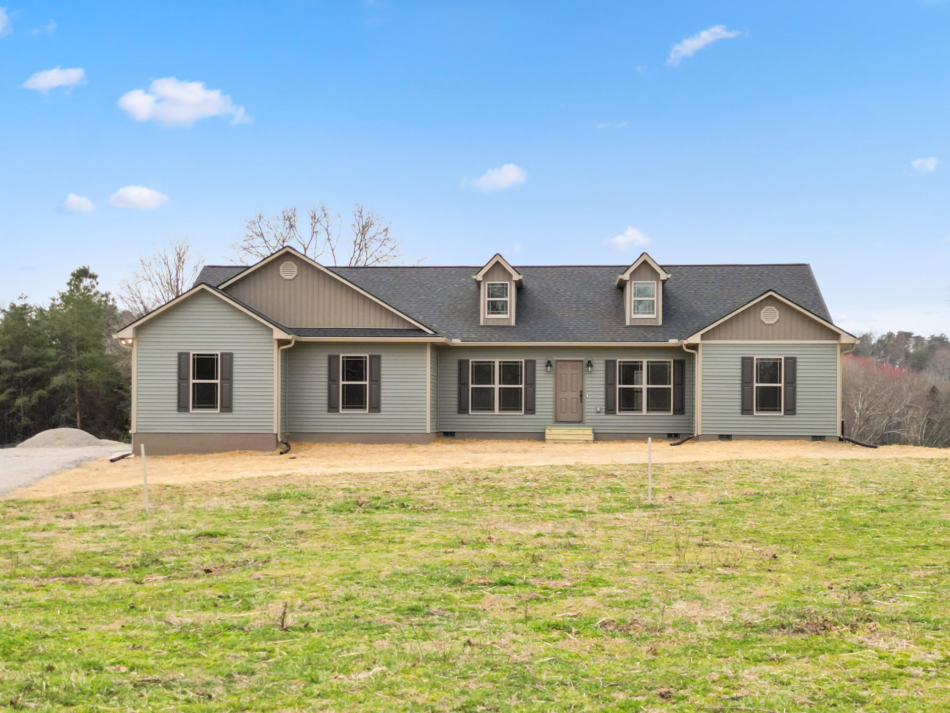 Two-story farmhouse with white siding, dormer window, black-handled white front door, and expansive green lawn under partly cloudy sky