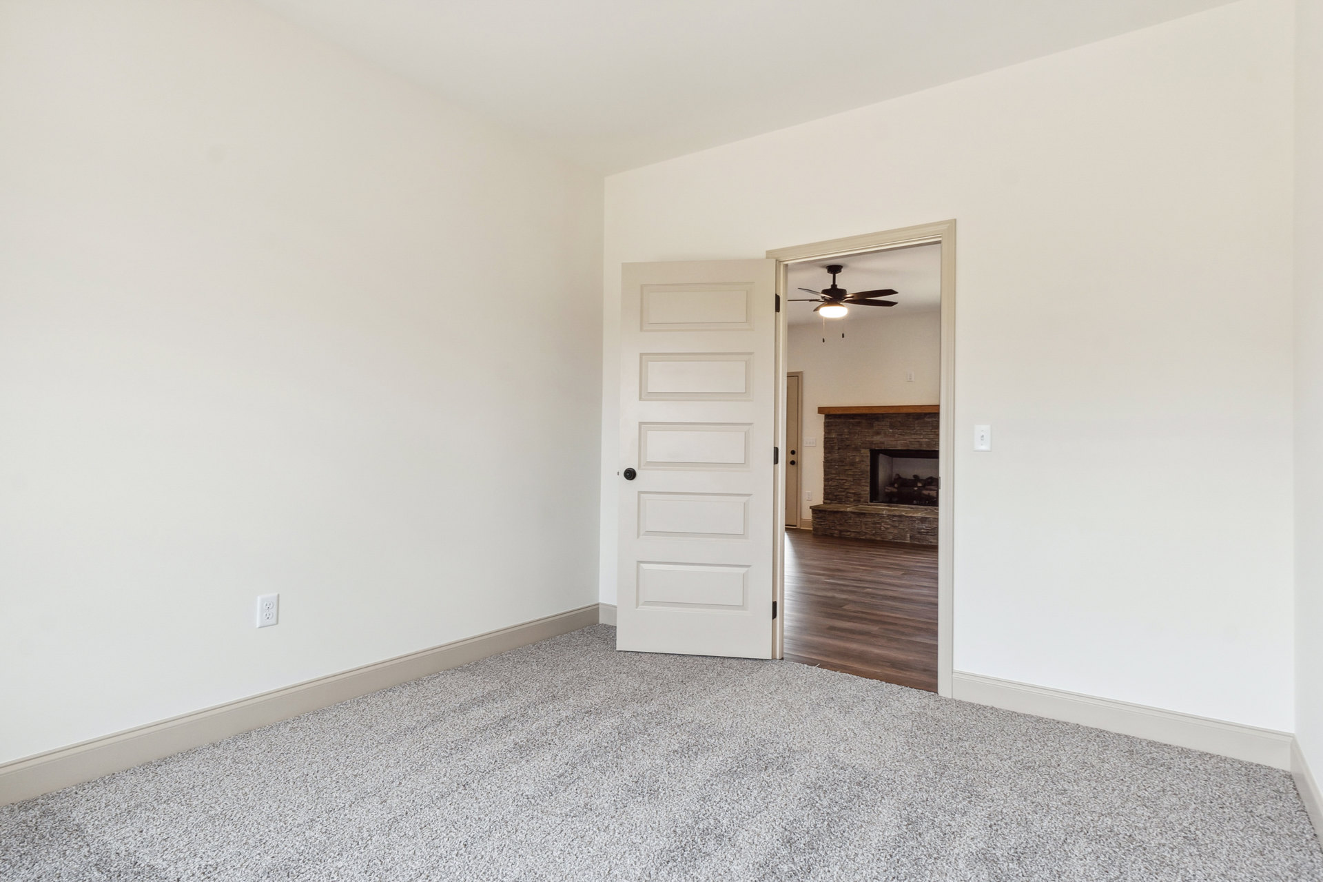 White paneled door with black knob open to living room featuring hardwood floors, stone accent wall, glass fireplace, and ceiling fan with light fixture.