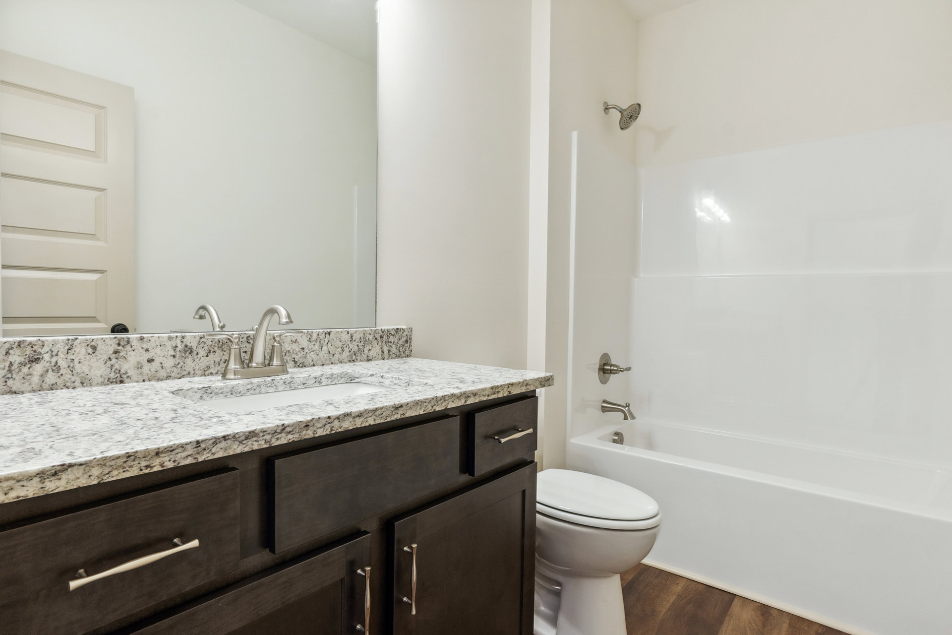 Bathroom with white tile floor, white toilet, rectangular sink set in a light-colored vanity, white paneled door, and bathtub partially visible.