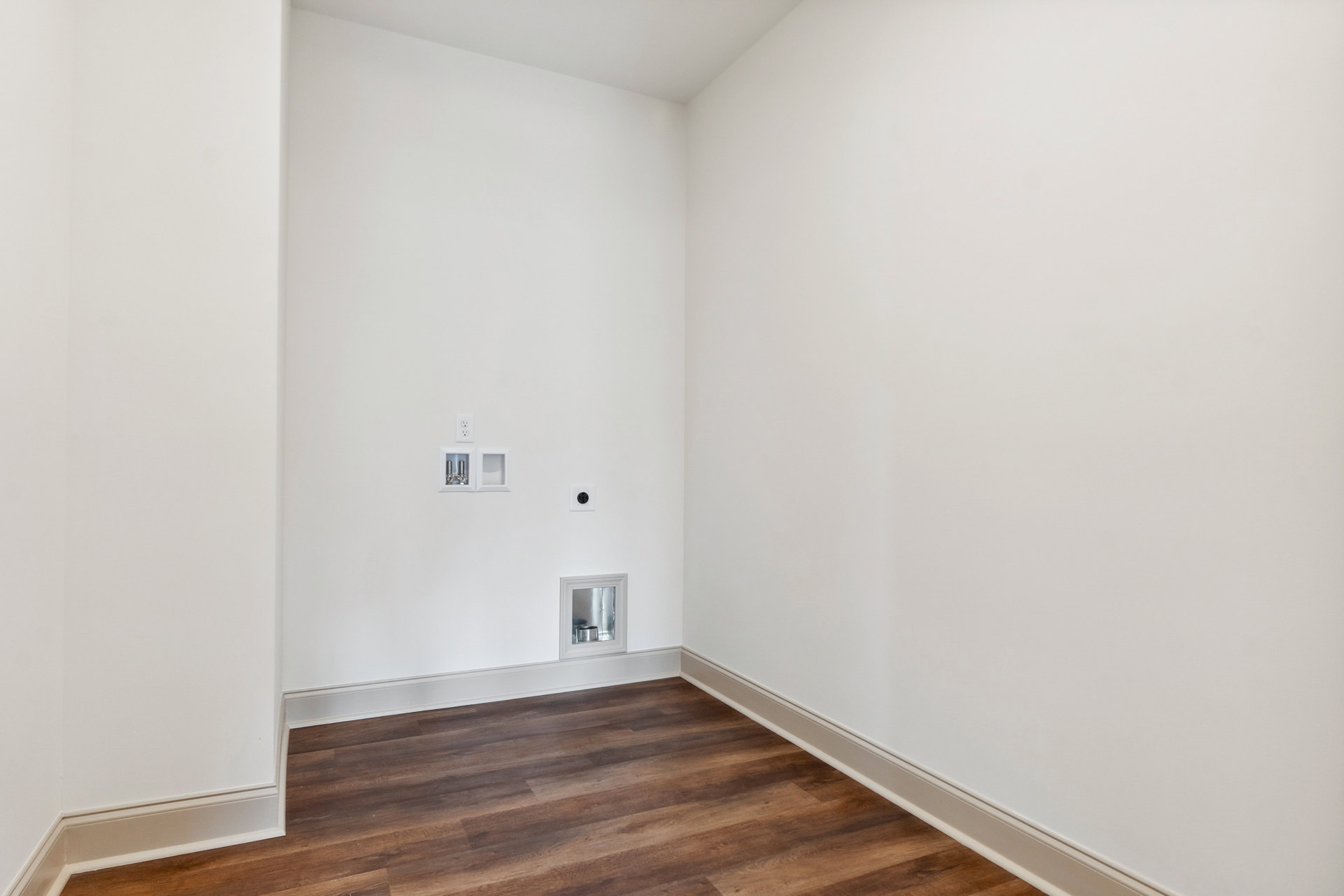 Wood flooring with white baseboards, white walls, and a white cabinet; small square objects mounted on the wall, silver container on the floor.
