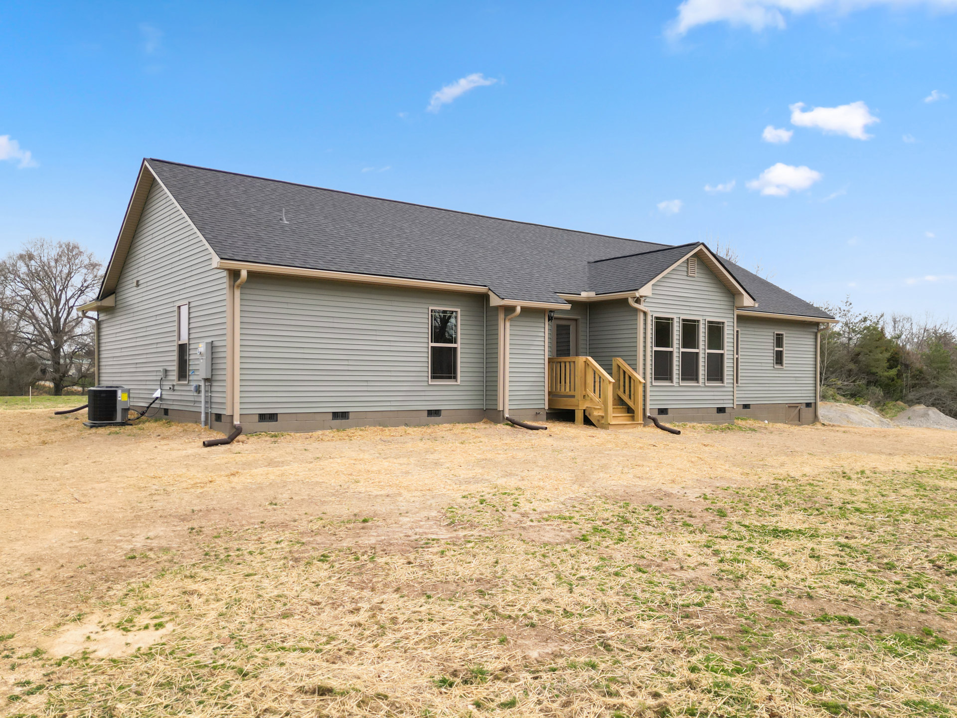 Two-story house with wood deck and stairs, grassy yard, leafless tree, large windows, and covered porch under cloudy sky