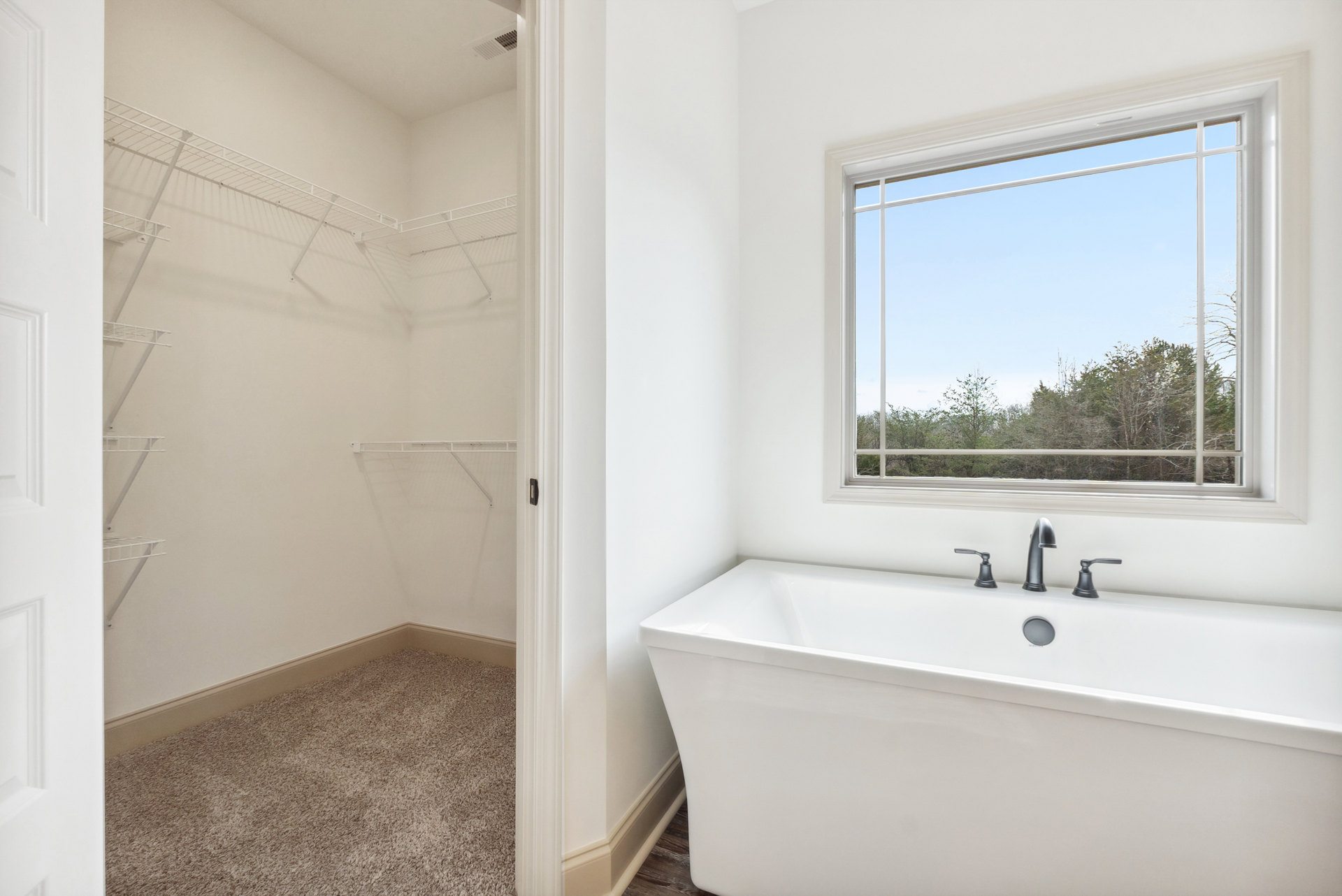 Bathroom with freestanding bathtub and glass-enclosed shower, white tile walls, modern sink with chrome faucets, large window overlooking trees, built-in closet with shelves and