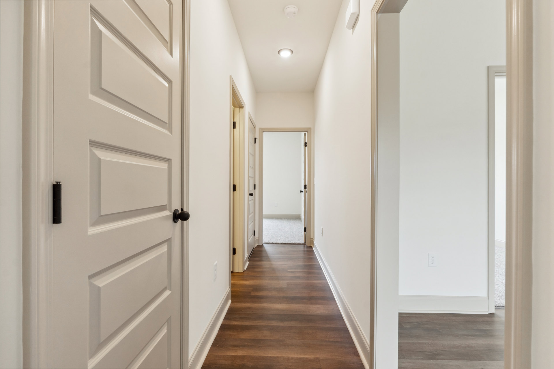 Hallway with white walls, hardwood floor, white door with black handle and white frame, ceiling molding