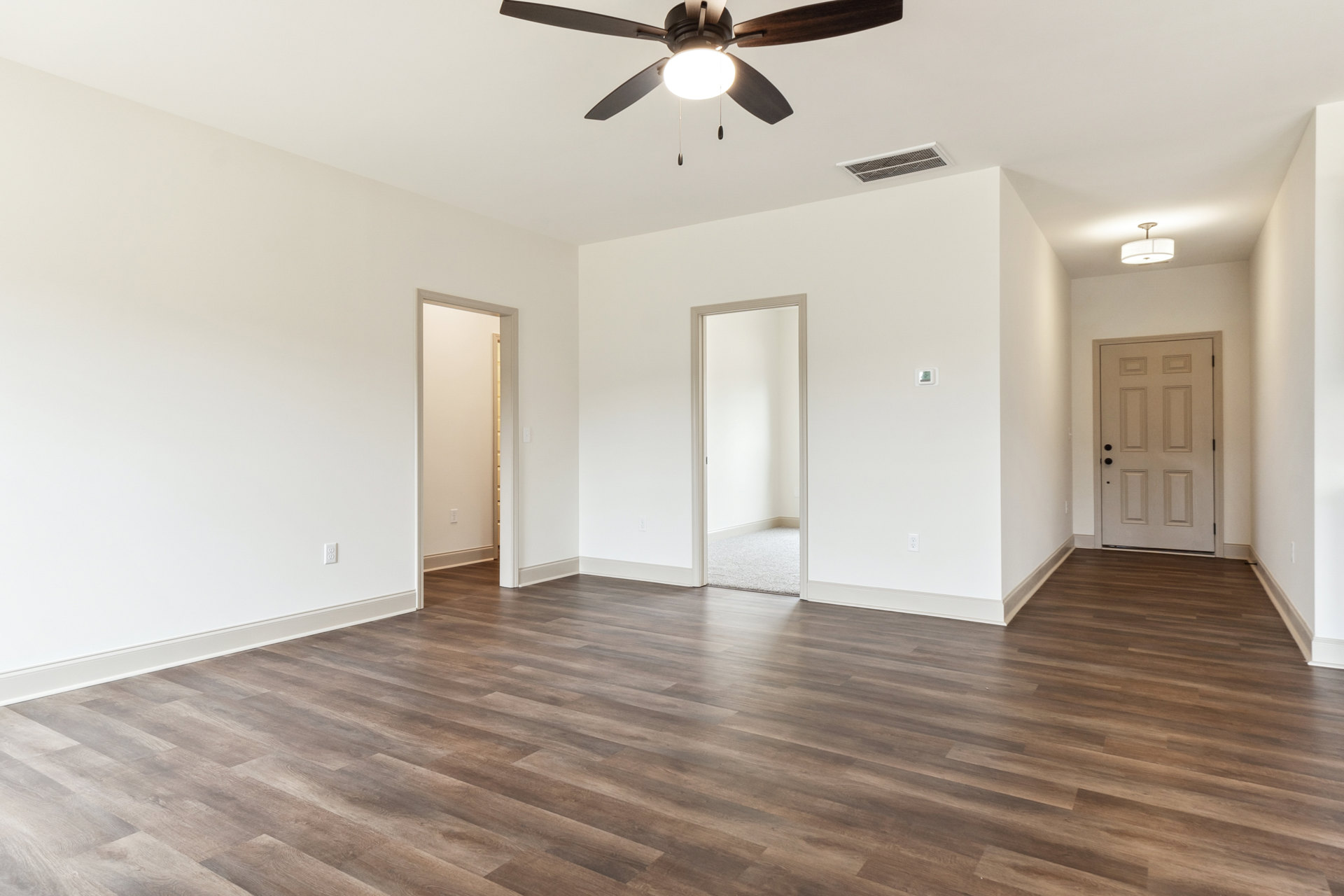 Ceiling fan with light fixture above wood flooring, white walls, and white door with black knobs and door frame