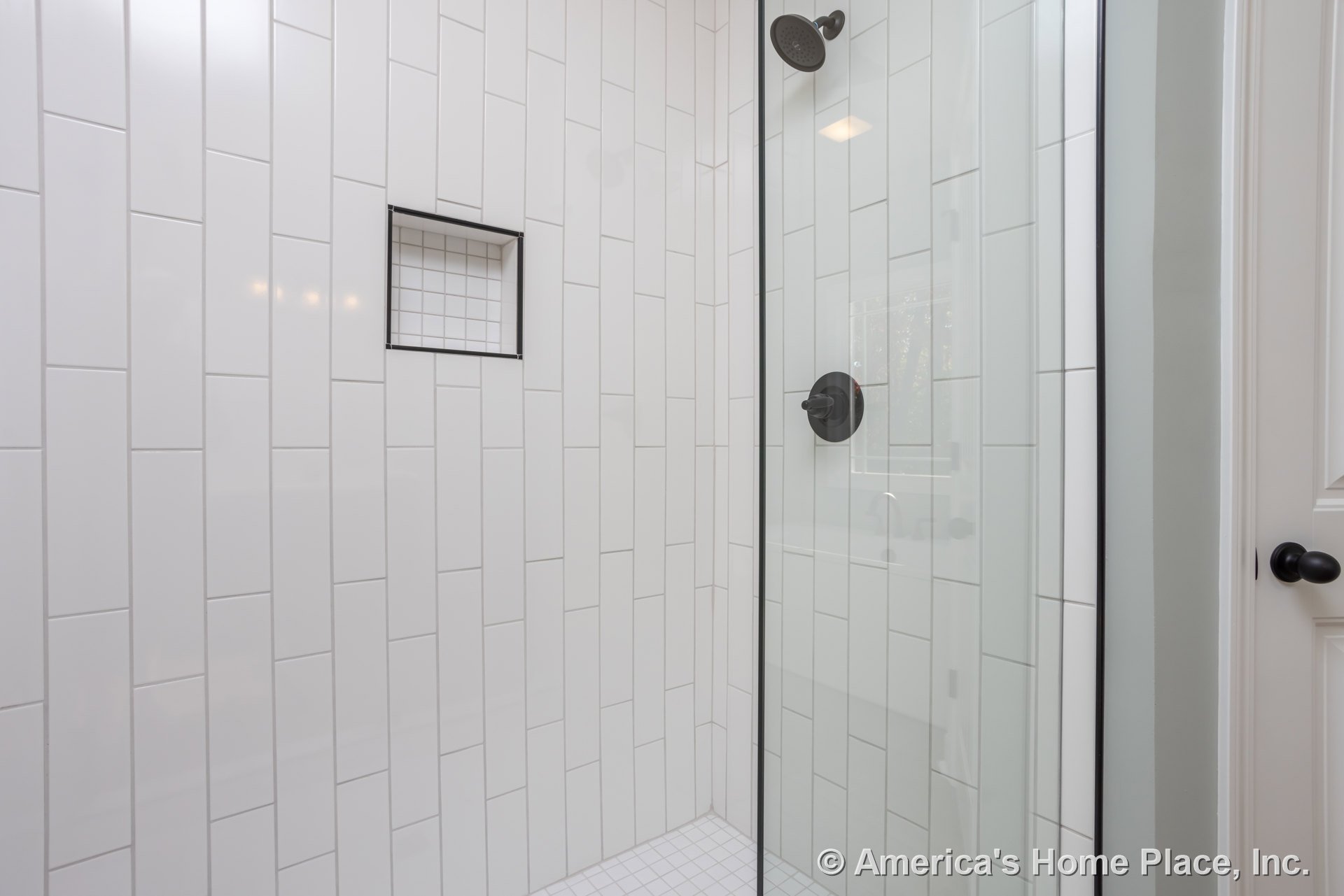 Shower with clear glass door, white tile walls and floor, black metal frame and door knob, round shower head