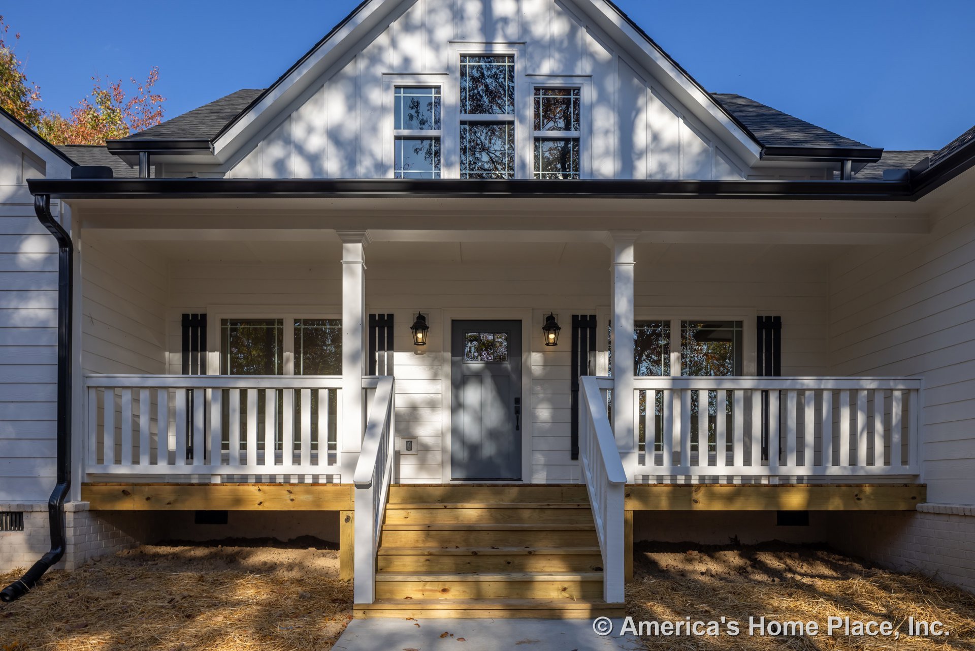 White house with multiple windows, grey front door with glass panel, wooden porch and steps, tree reflections visible in window glass, light-colored siding exterior