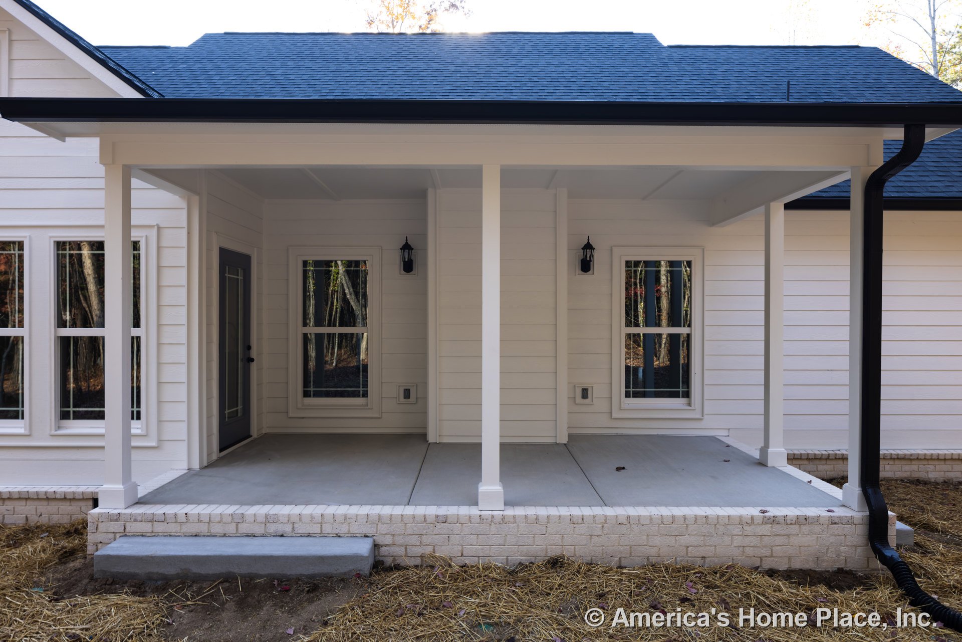 White siding house with covered porch, white framed windows, glass door, and gabled roof surrounded by trees