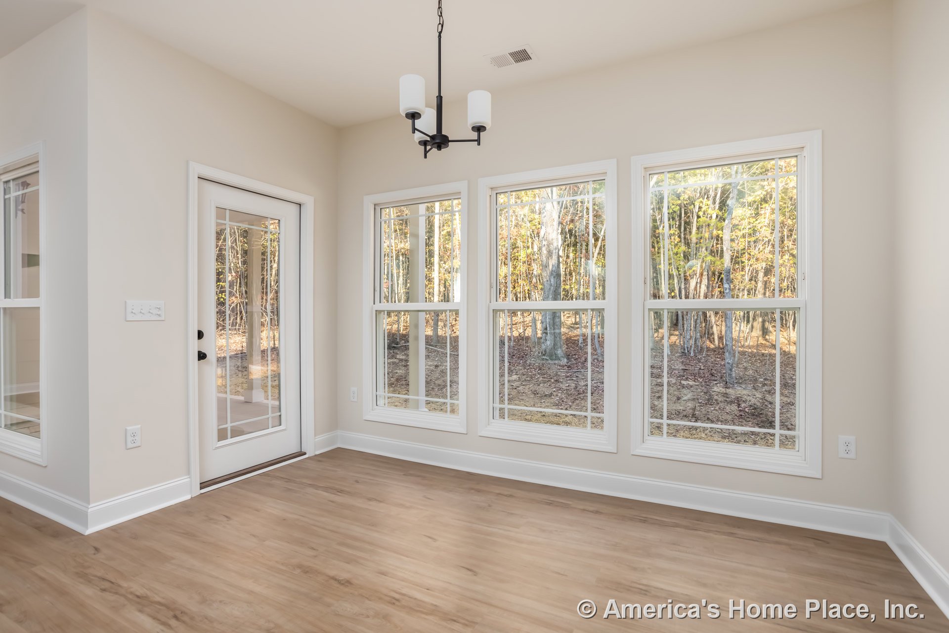 Wood flooring and white walls in a bright room with large windows and a door overlooking a forested landscape