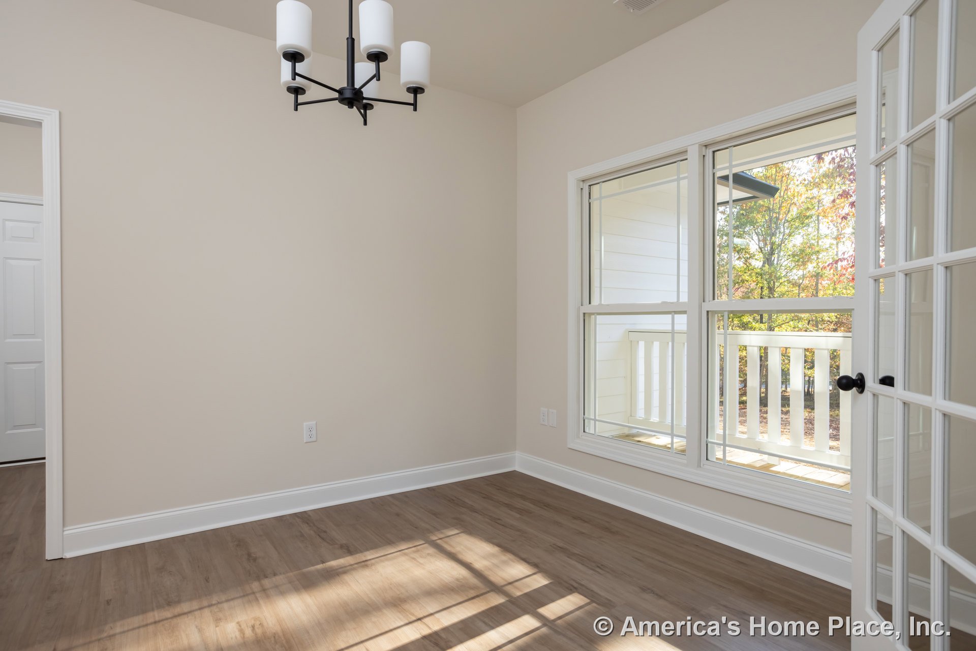 Chandelier with black and white accents hanging above wood laminate flooring, large window framed by white molding, white walls, and a black base light fixture