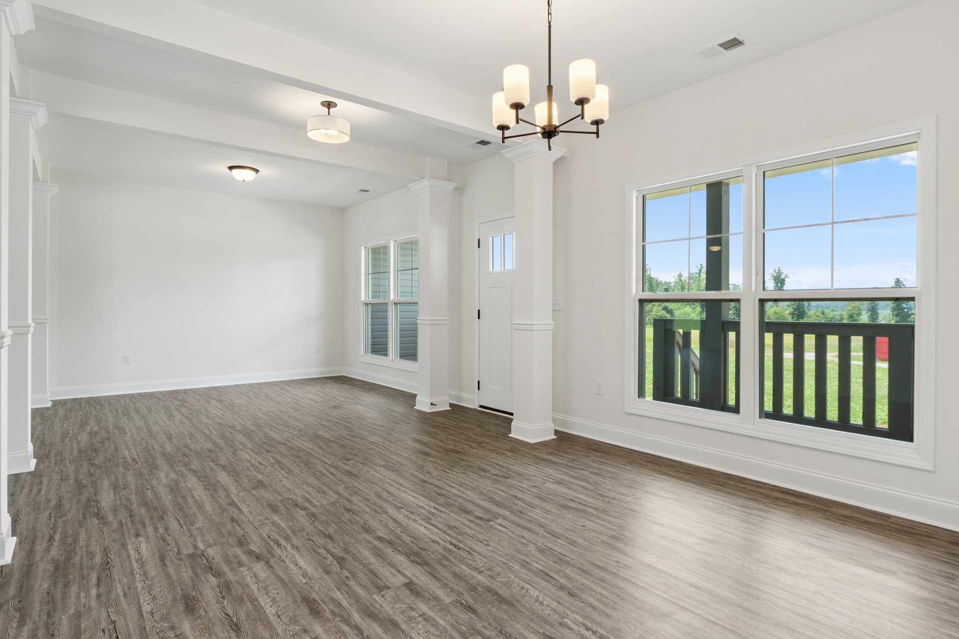 Wood flooring in a spacious room with white pillars, large windows, and an ornate chandelier hanging from the ceiling