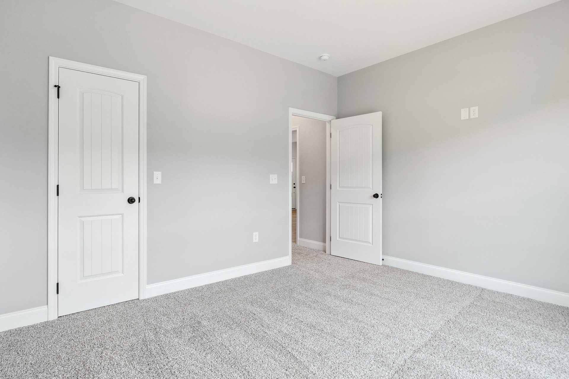 White carpeted room with white paneled door featuring a black knob, white walls, and smooth ceiling.