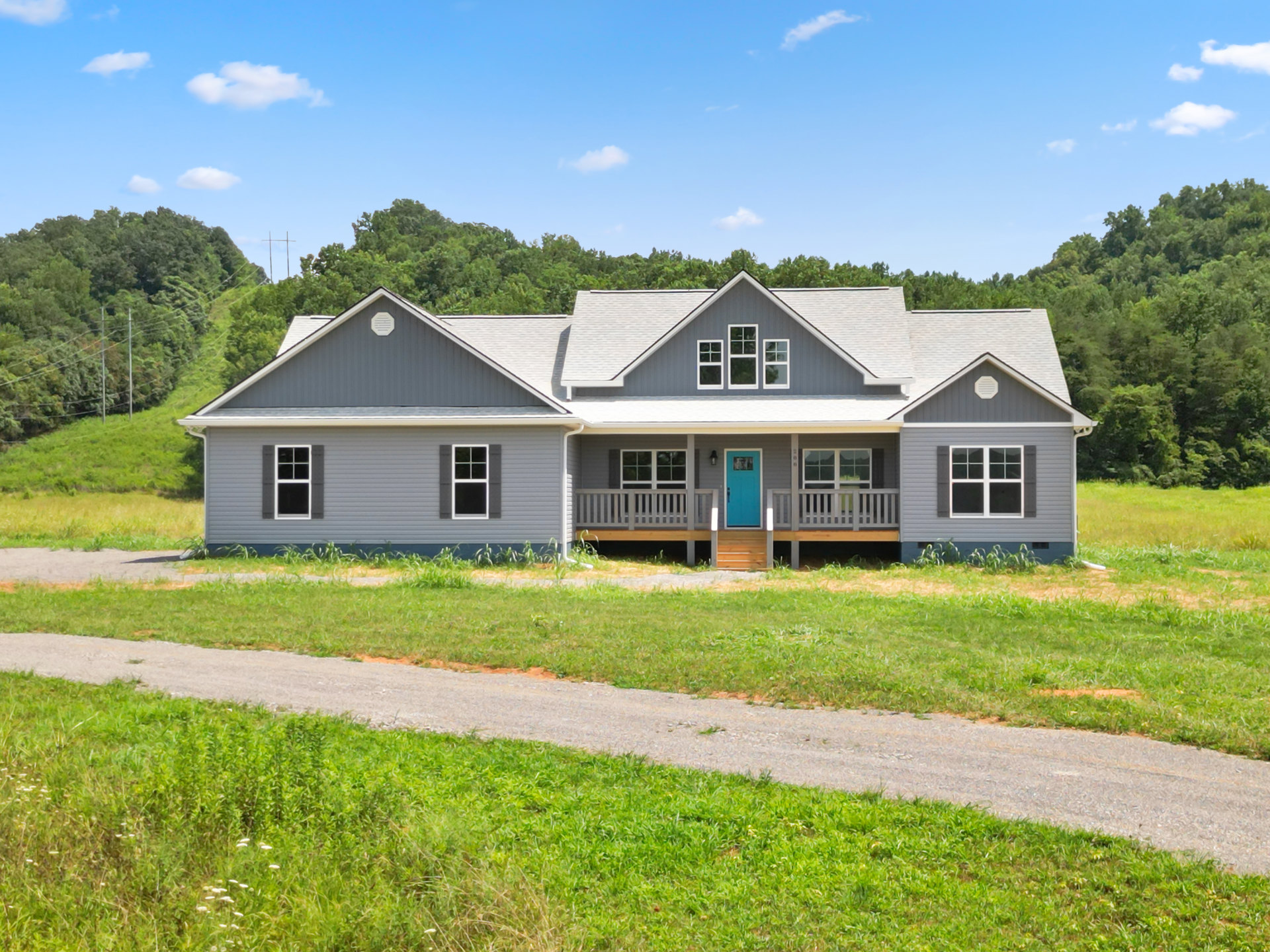 Two-story house with blue front door, white-framed windows, covered porch, green lawn, and mature trees under a partly cloudy sky