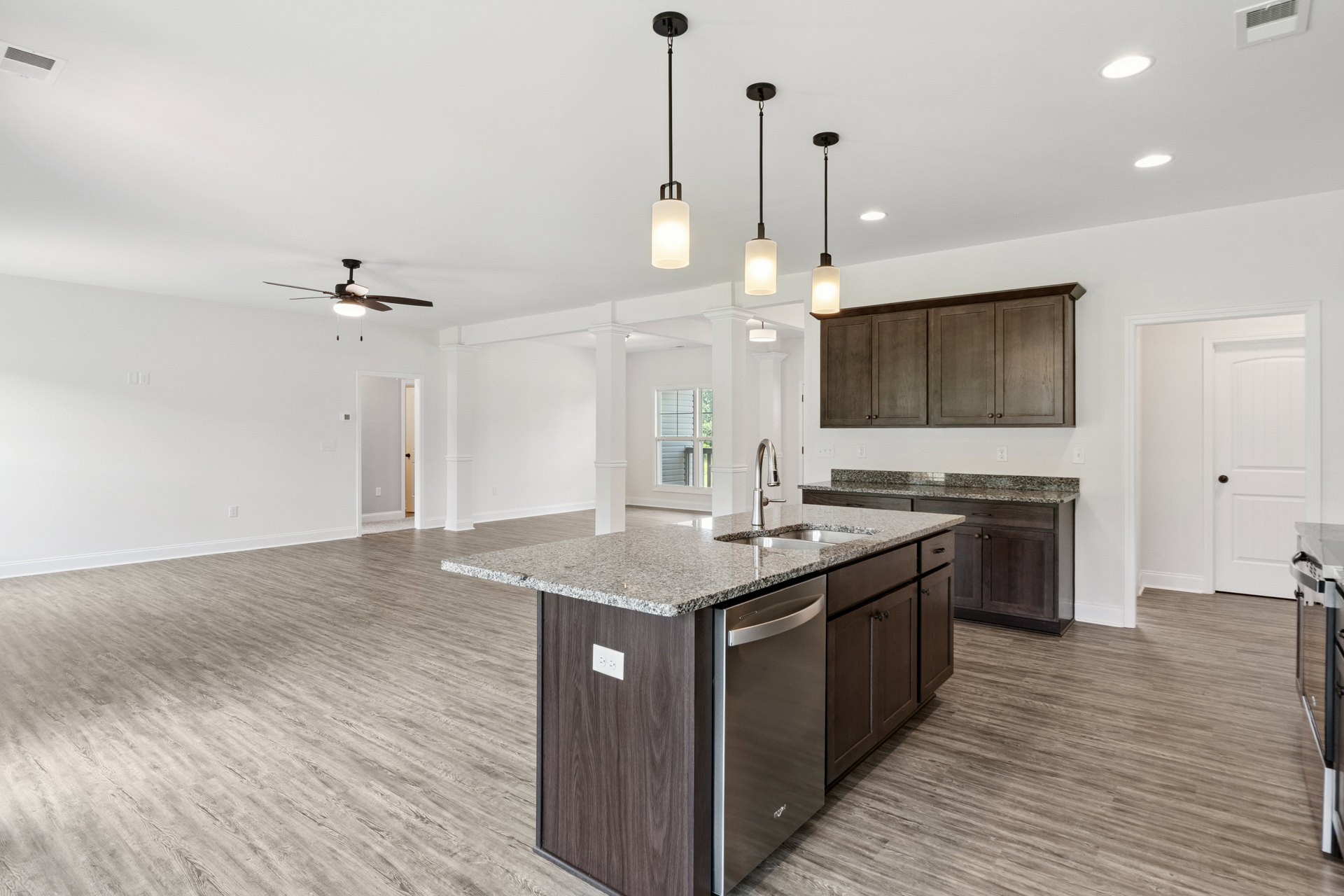 Spacious kitchen featuring a large central island with stone countertop, built-in sink and dishwasher, white cabinetry, tile flooring, and modern wall lighting.