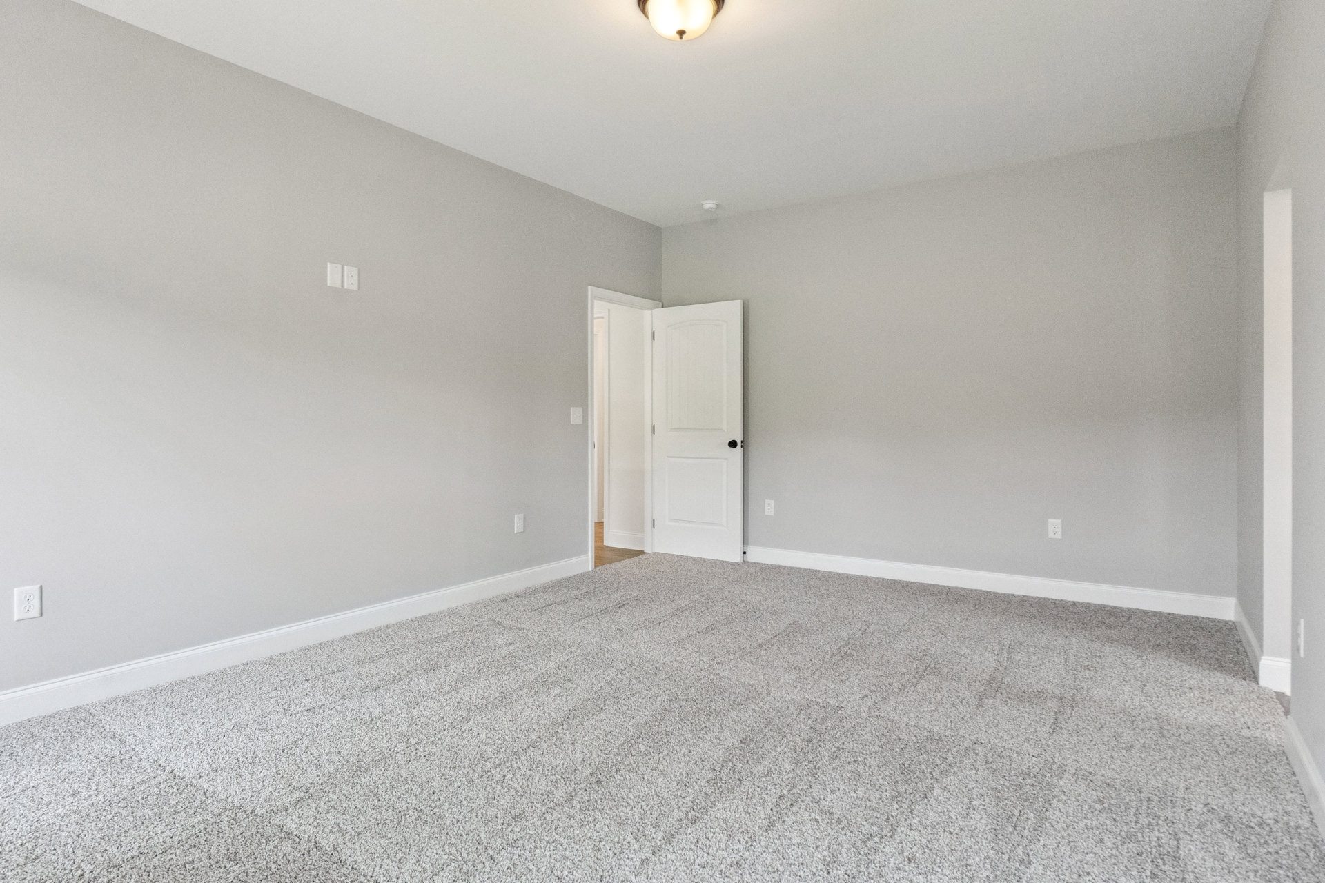 Carpeted room with white paneled door featuring black hardware, light fixture on ceiling, smooth plaster walls, and baseboard trim